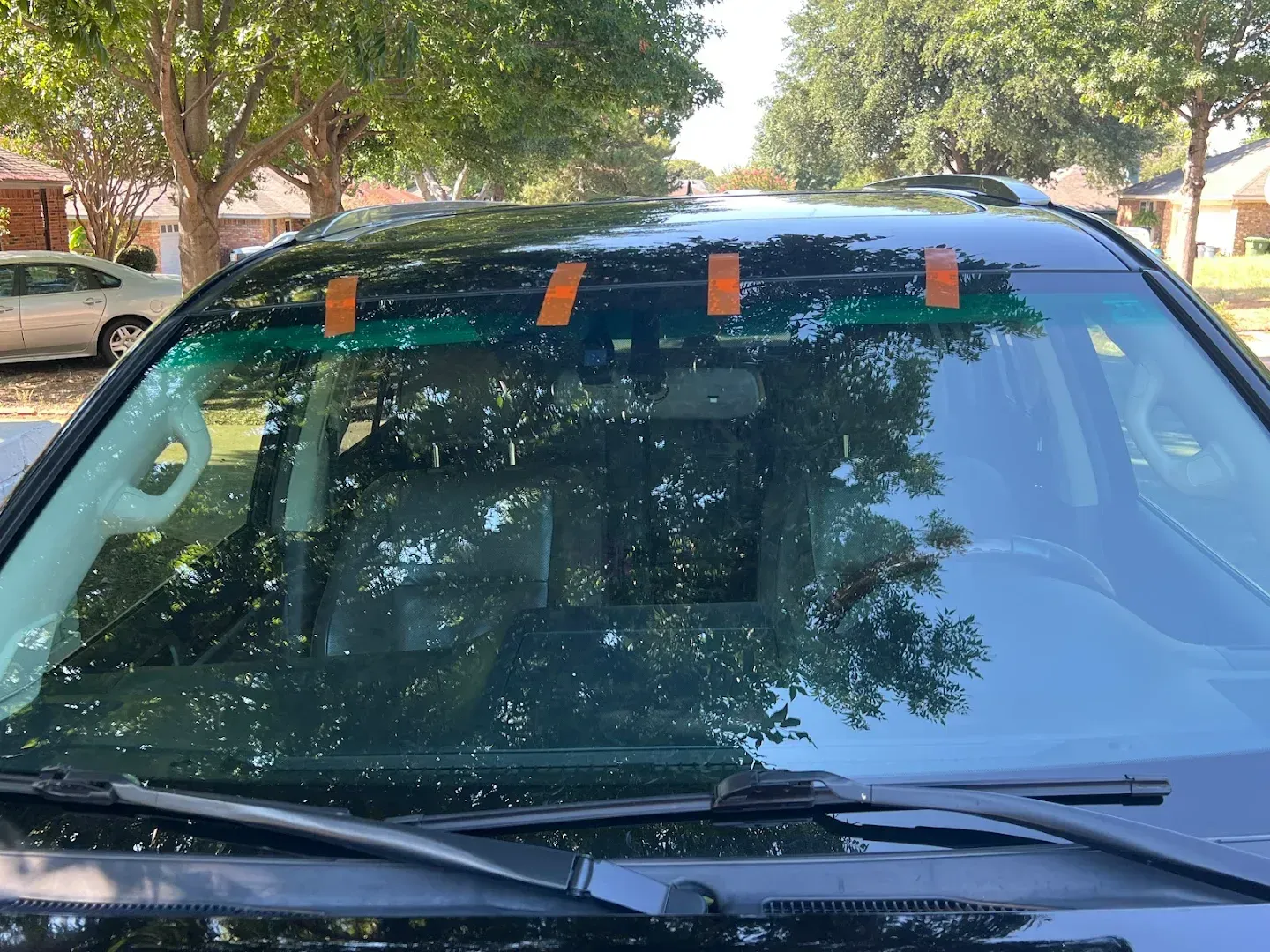 Windshield of a black car with orange tape holding something in place, parked outdoors.