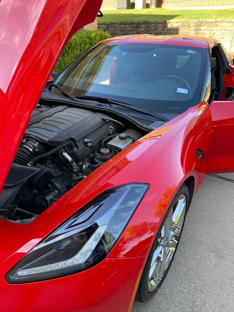 Bright red sports car with the hood and door open, parked outside.