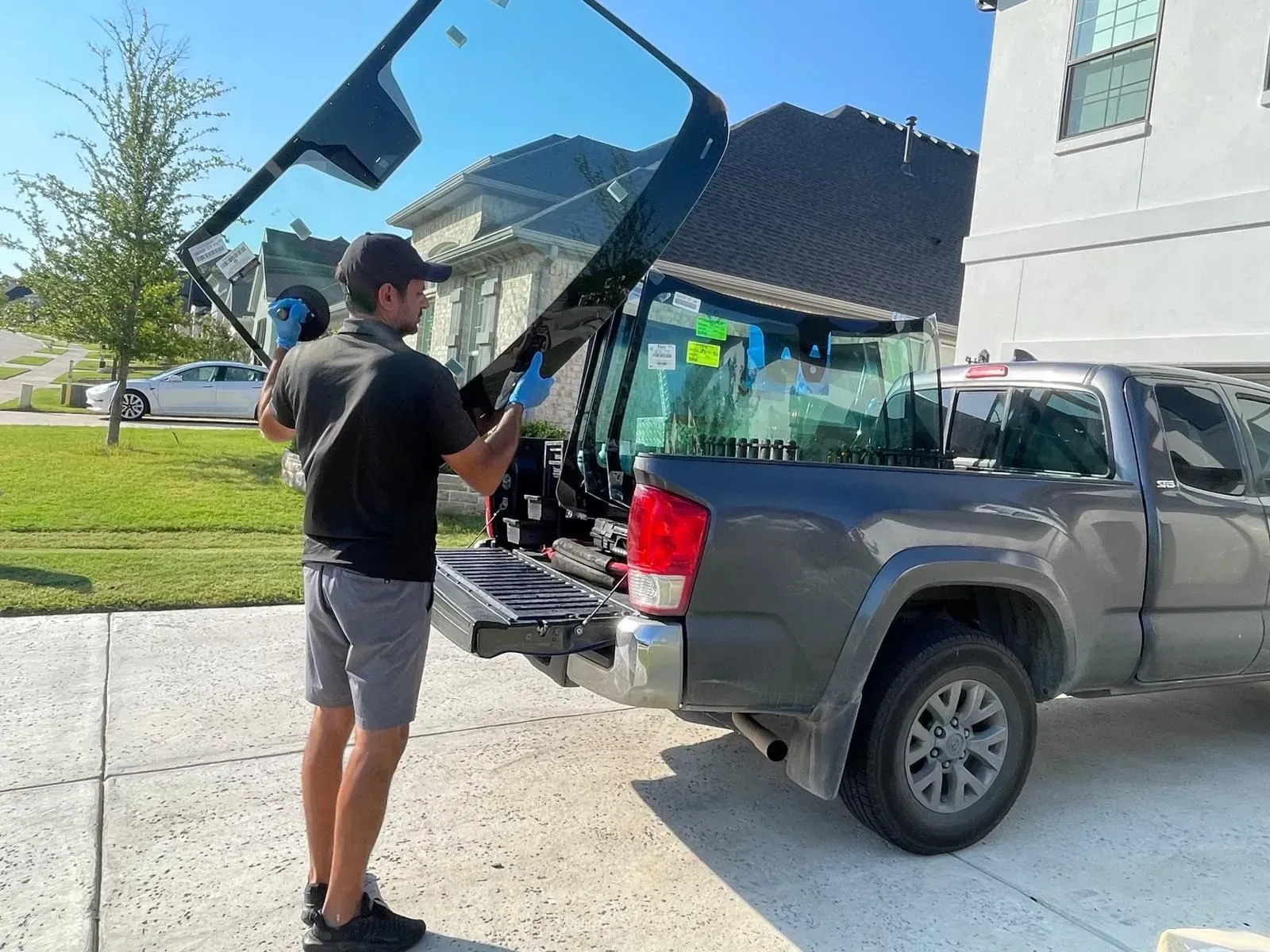 Man holding a truck window, standing next to a gray pickup truck in a suburban driveway.