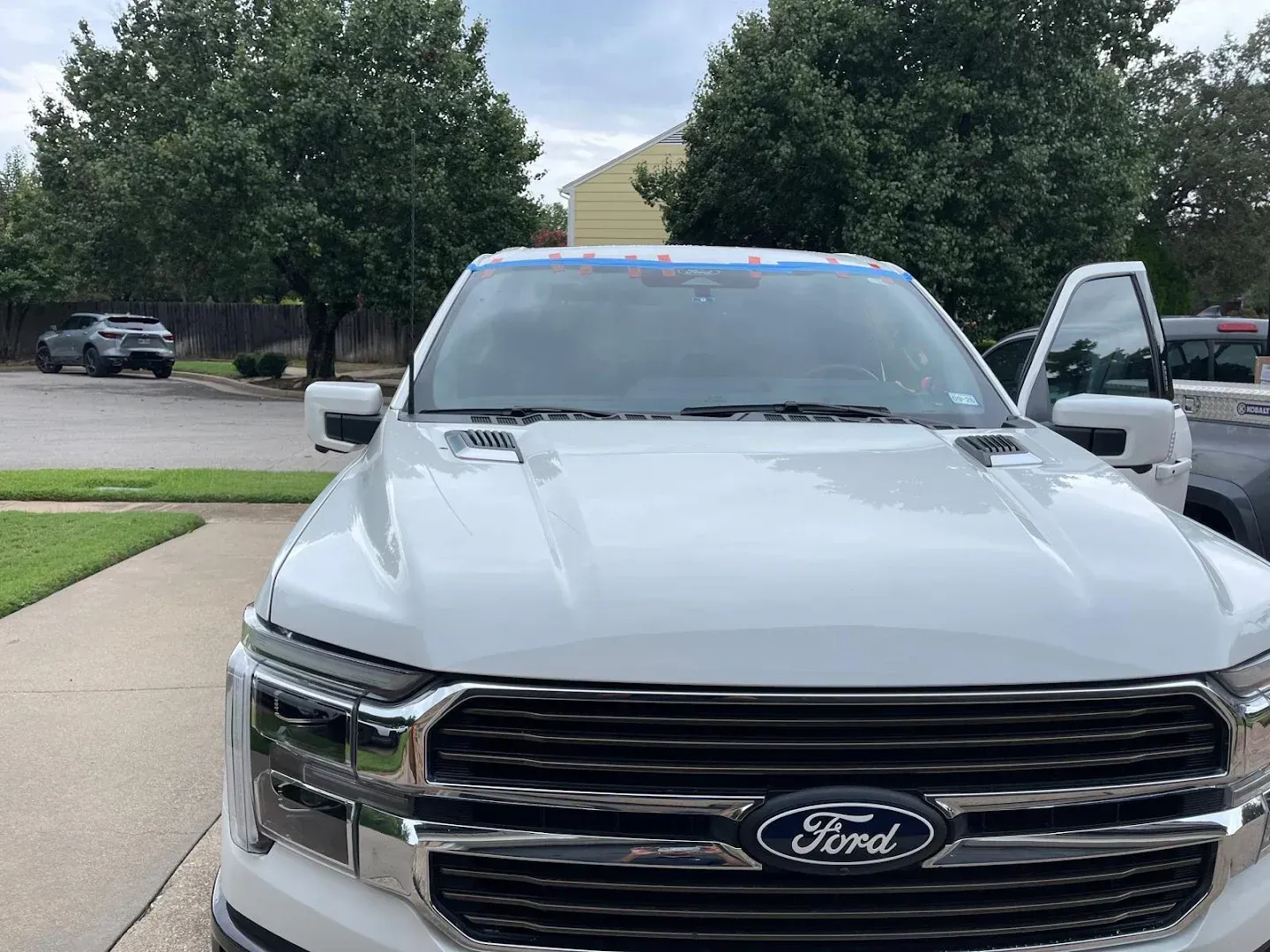 White Ford truck parked in front of a house, with an open door, on a cloudy day.
