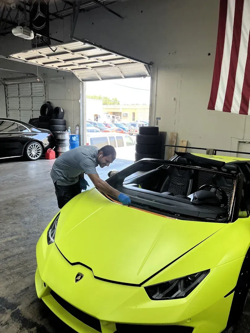 Man cleaning neon yellow Lamborghini in a garage, American flag in the background.