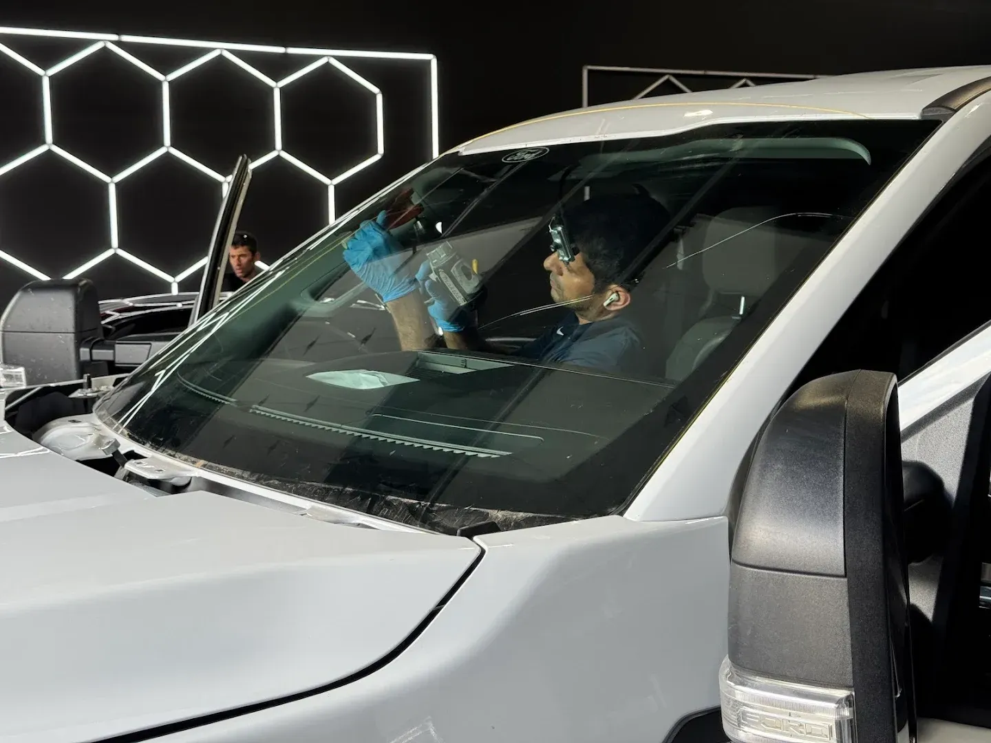 Person in a car getting the windshield cleaned; white vehicle, black background with a hexagon-shaped light.