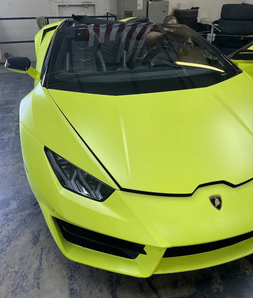 Dark gray car with shattered windshield; doors open in a garage.