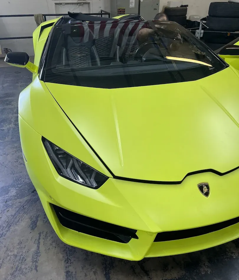 Black car with open door and wet windshield; orange tape on the glass.
