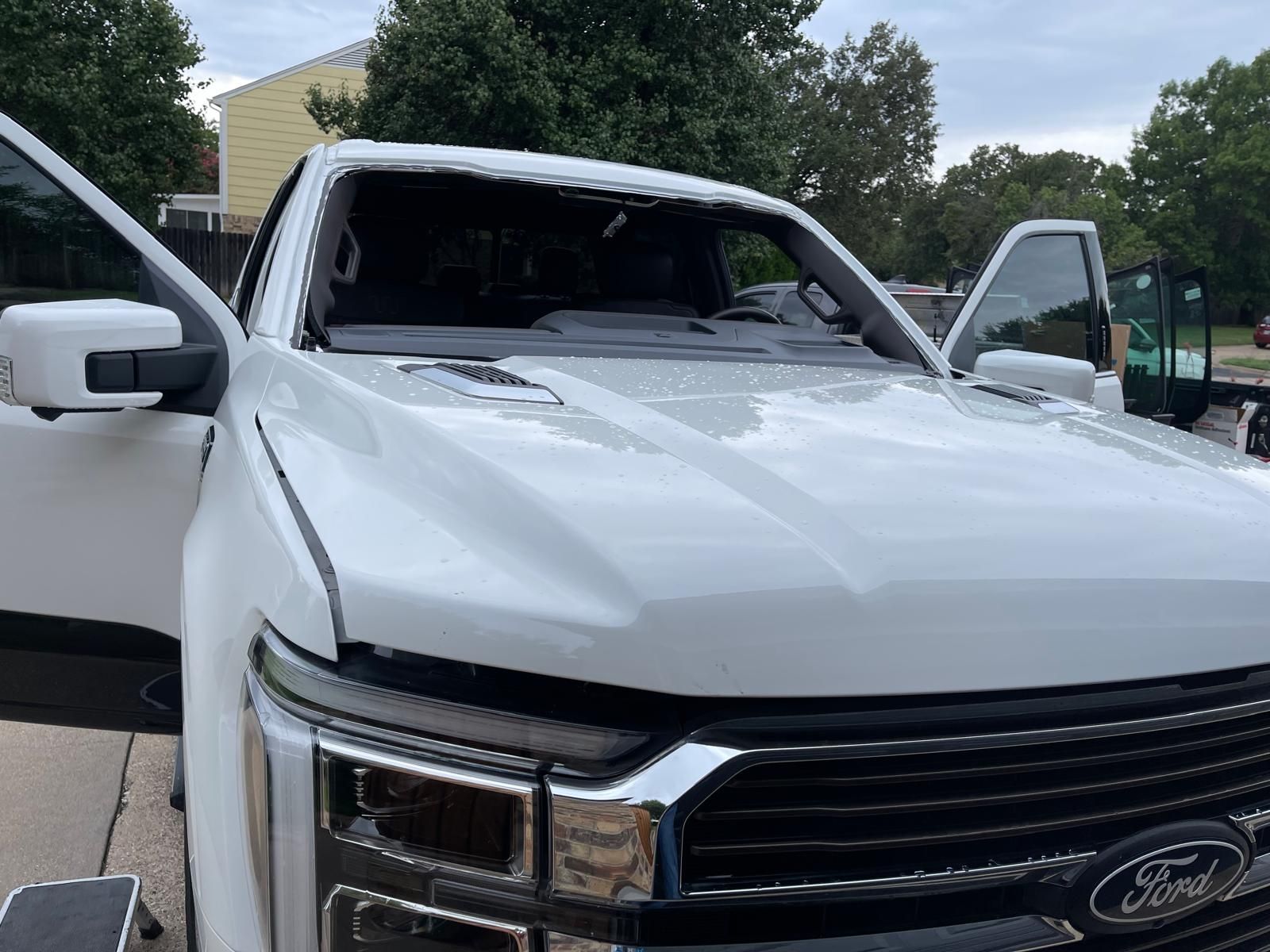 White Ford pickup truck with broken windshield, doors open, parked outside.