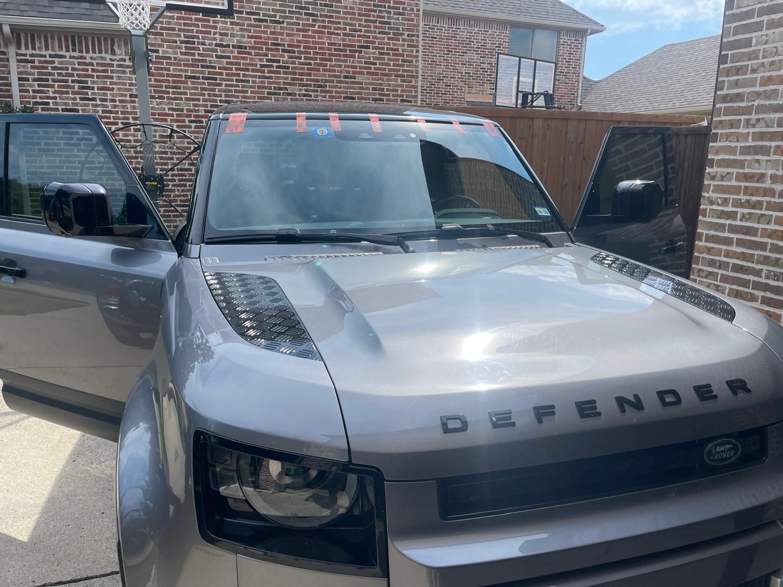 Gray car with shattered driver's side window, parked outside a building on a sunny day.