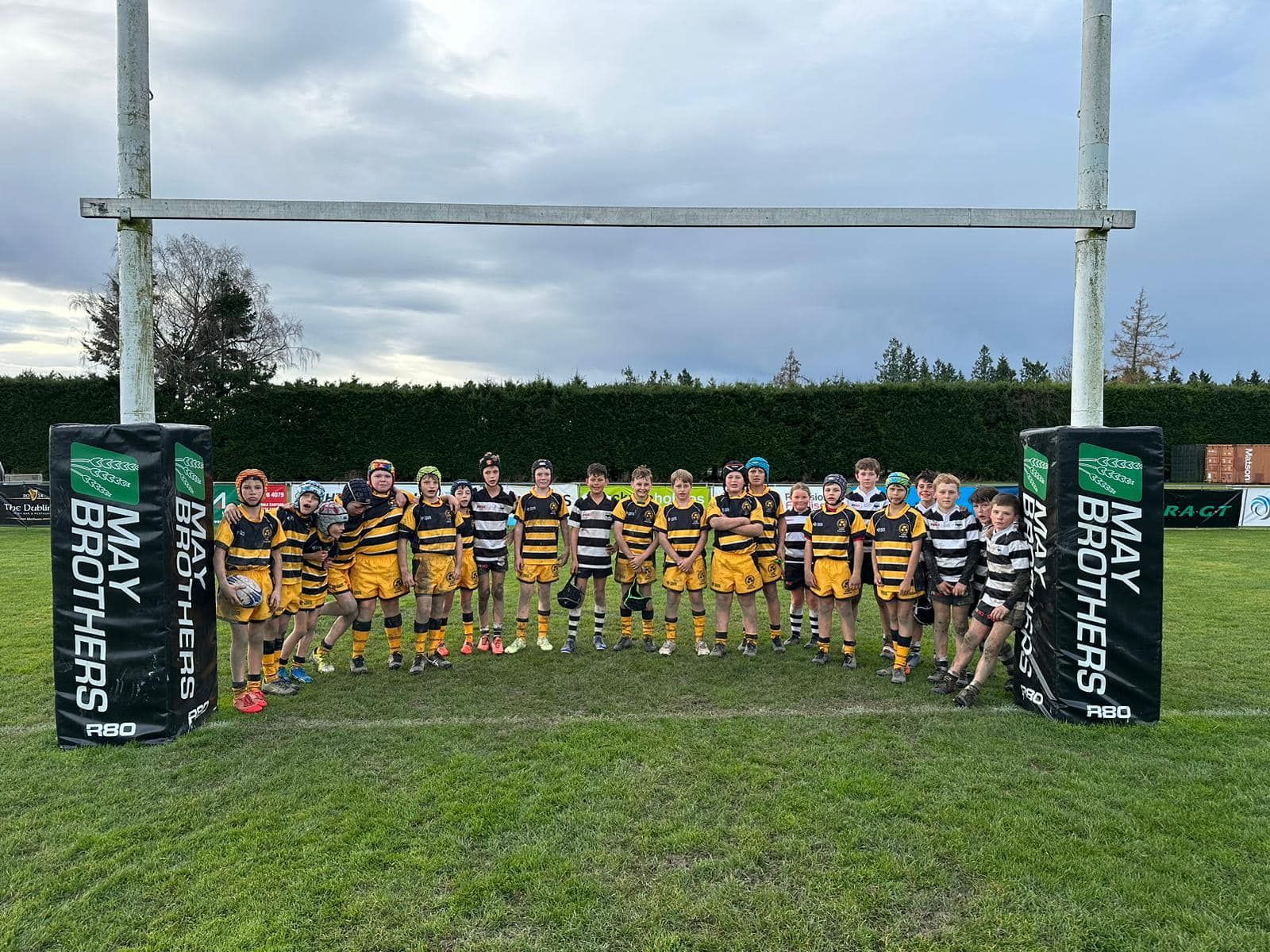 A group of rugby players standing in front of a goal with a may brothers sign