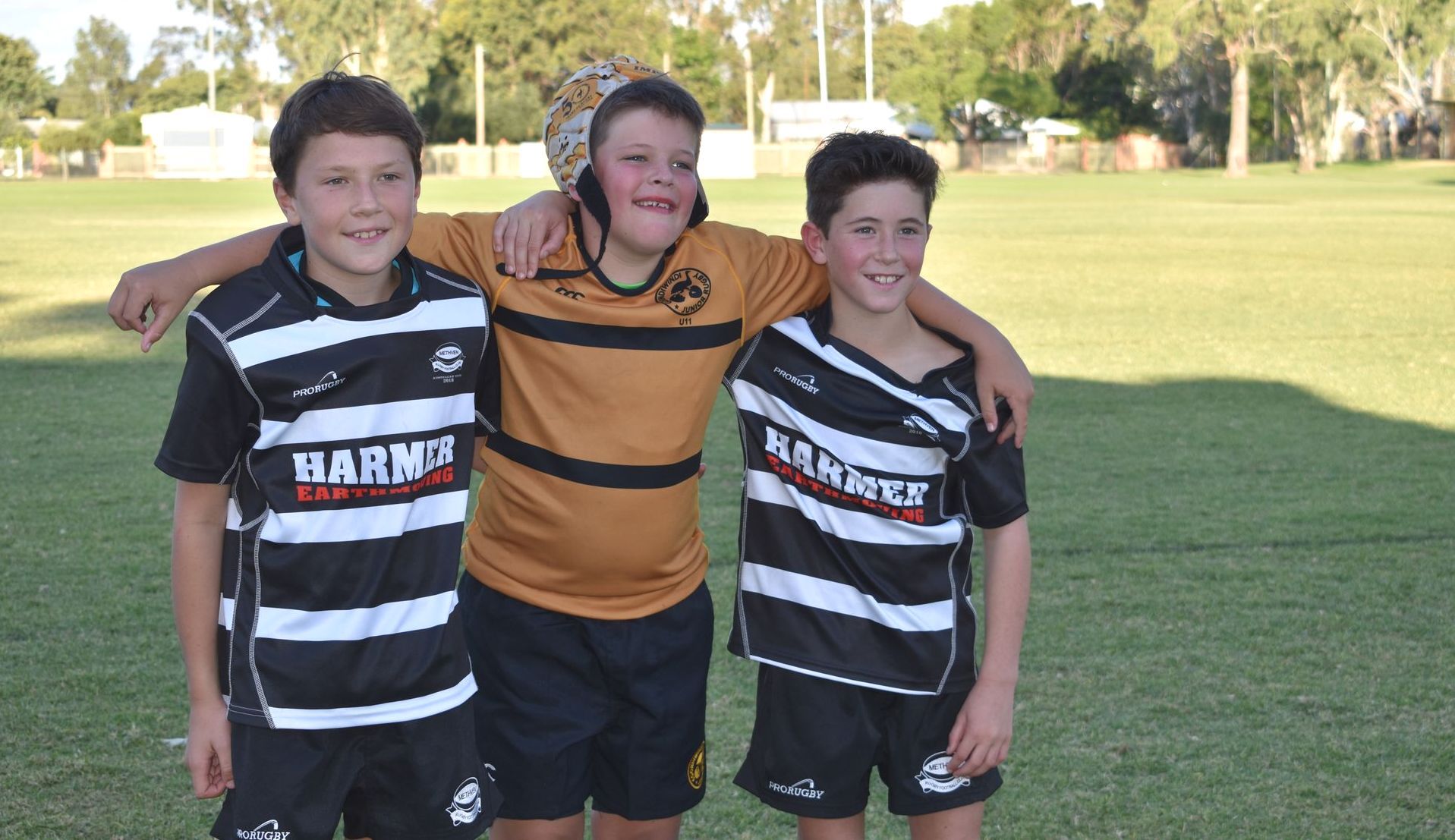 Three boys are posing for a picture with one wearing a shirt that says ' baby ' on it
