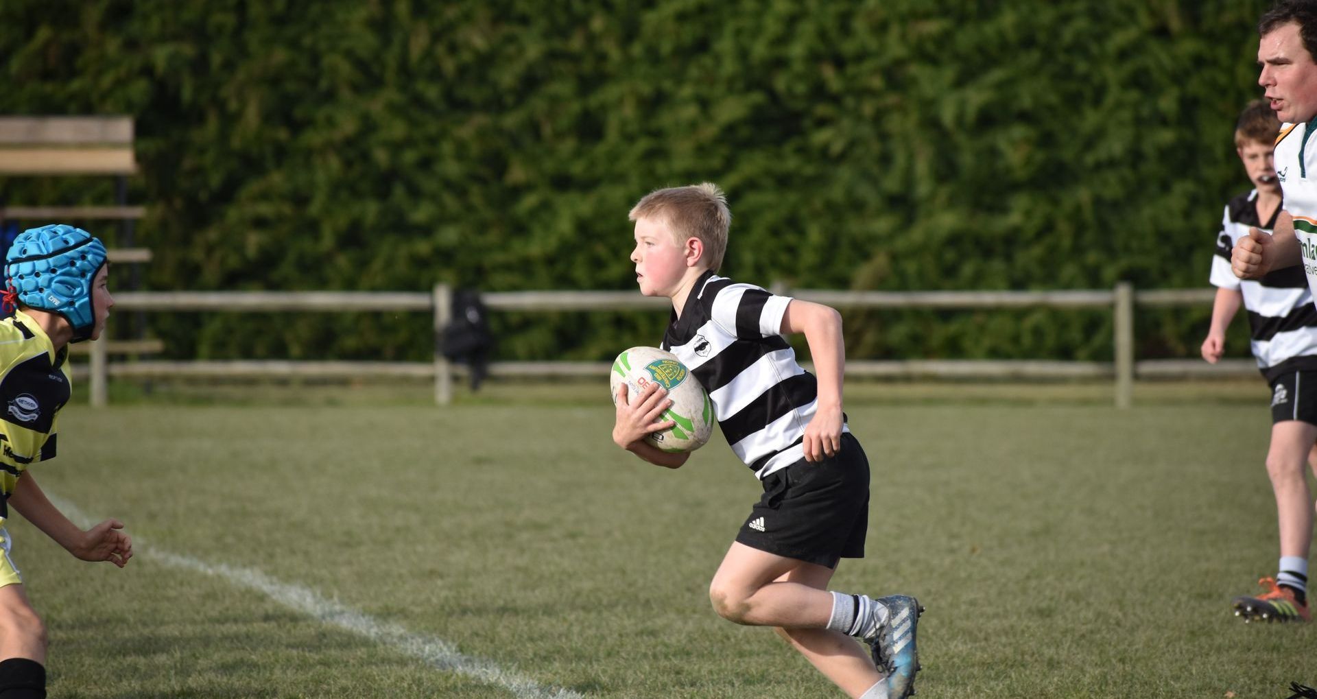 A young boy is running with a rugby ball on a field