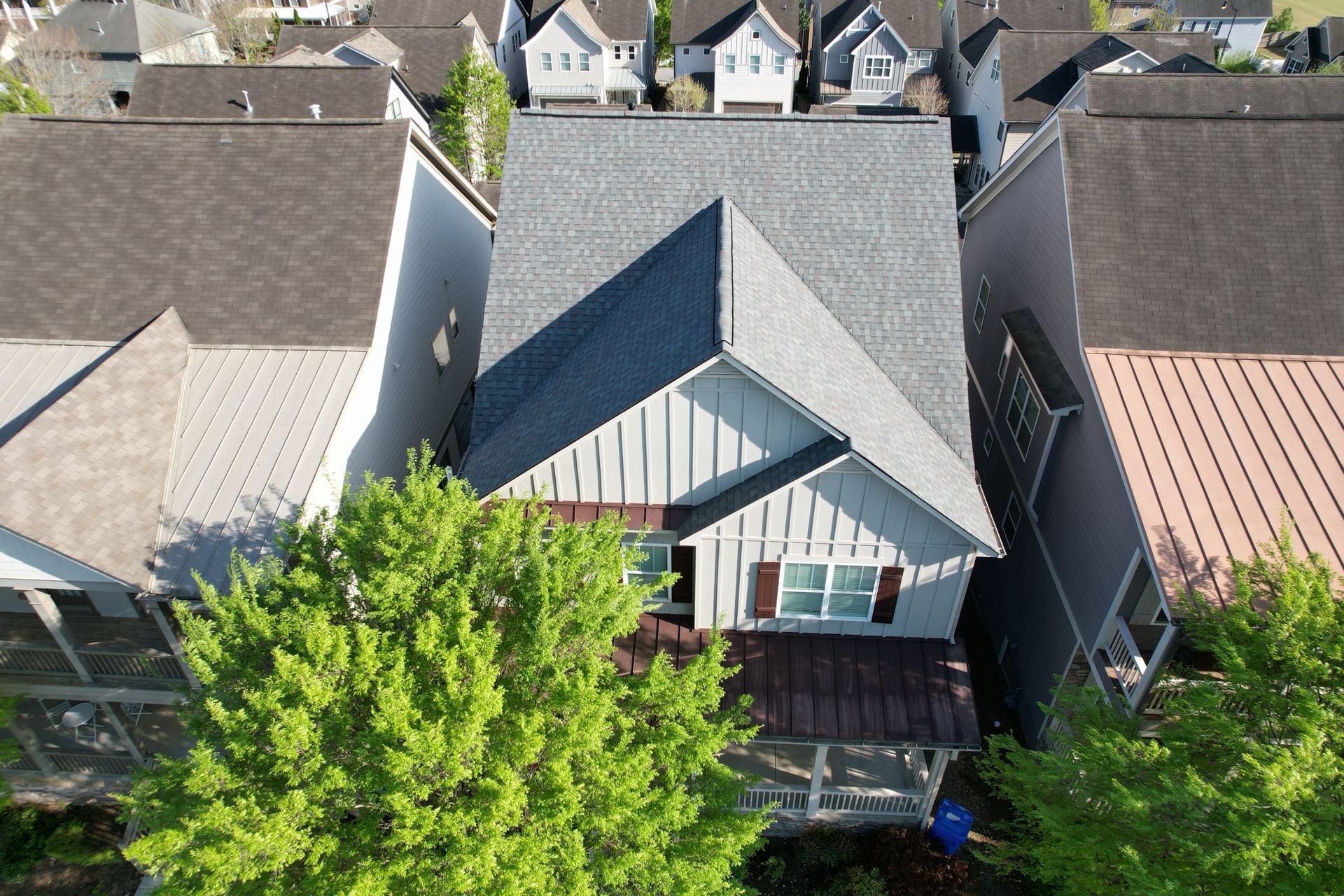 Aerial view of a gray-roofed residential house nestled between two neighboring homes, surrounded by trees.