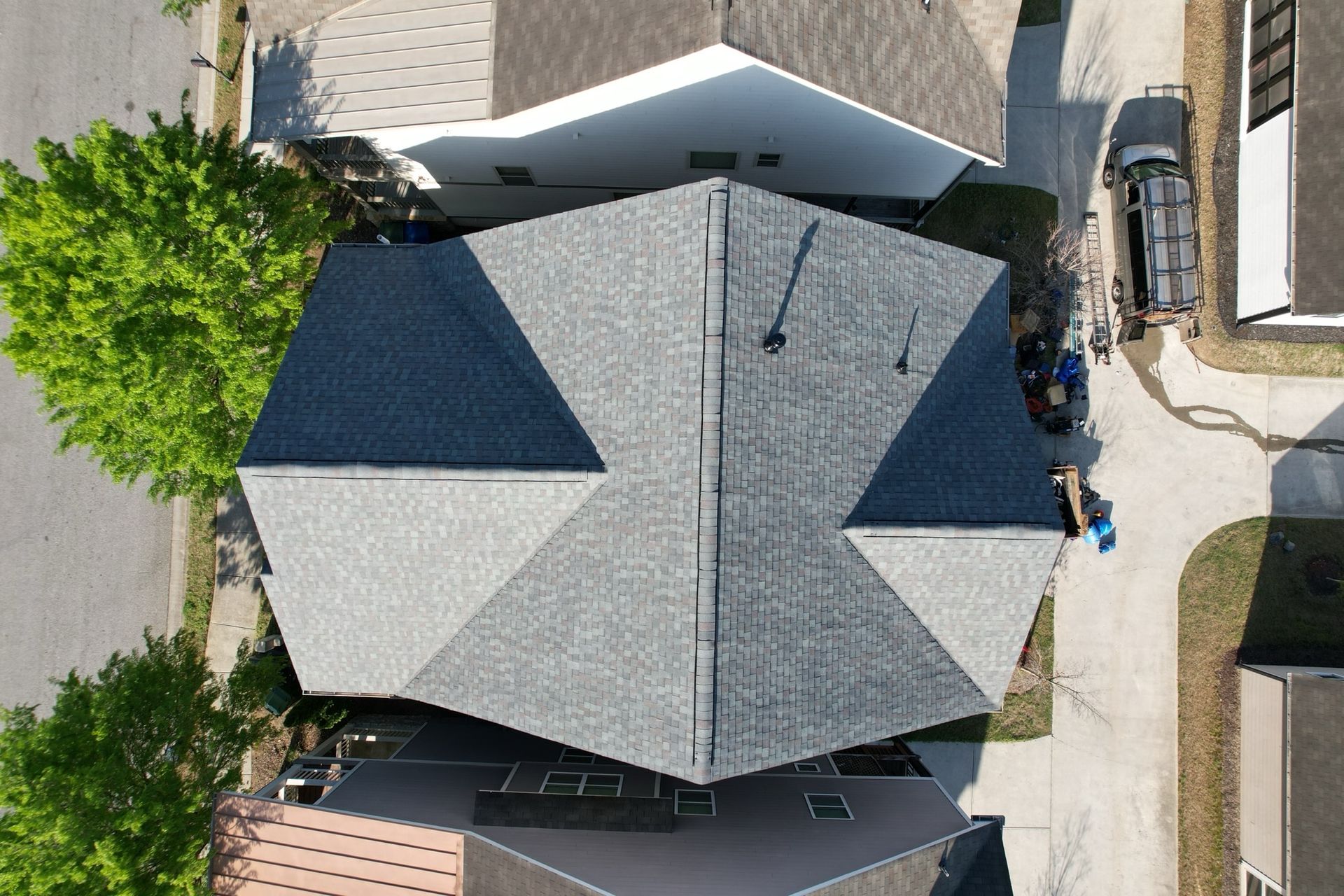 Aerial view of a residential house roof with a mix of new charcoal and weathered gray shingles.