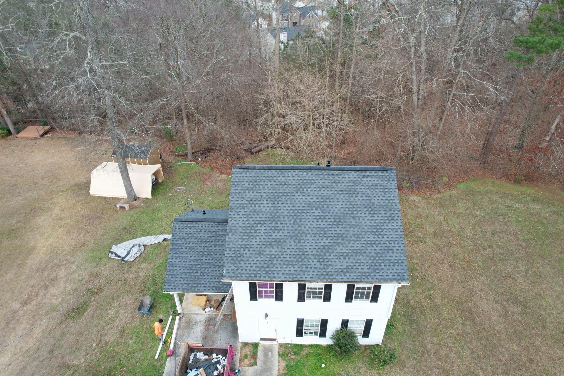 Aerial view of a white two-story house with a grey roof, set on a rural property with a shed and trees nearby.