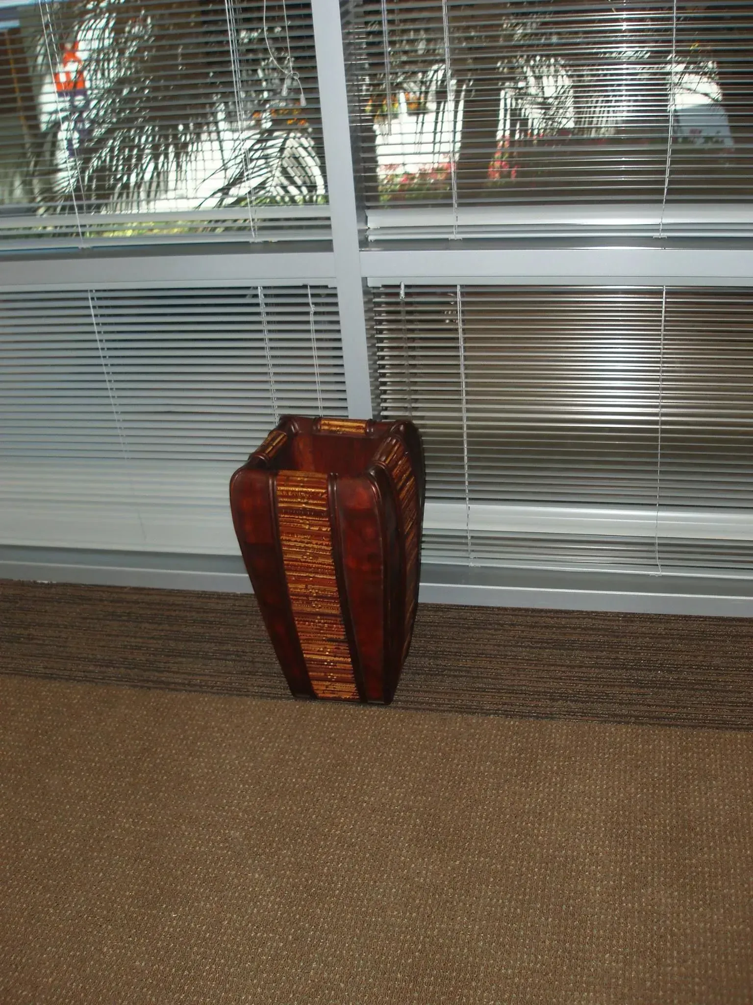 Brown wooden vase near a window with blinds.