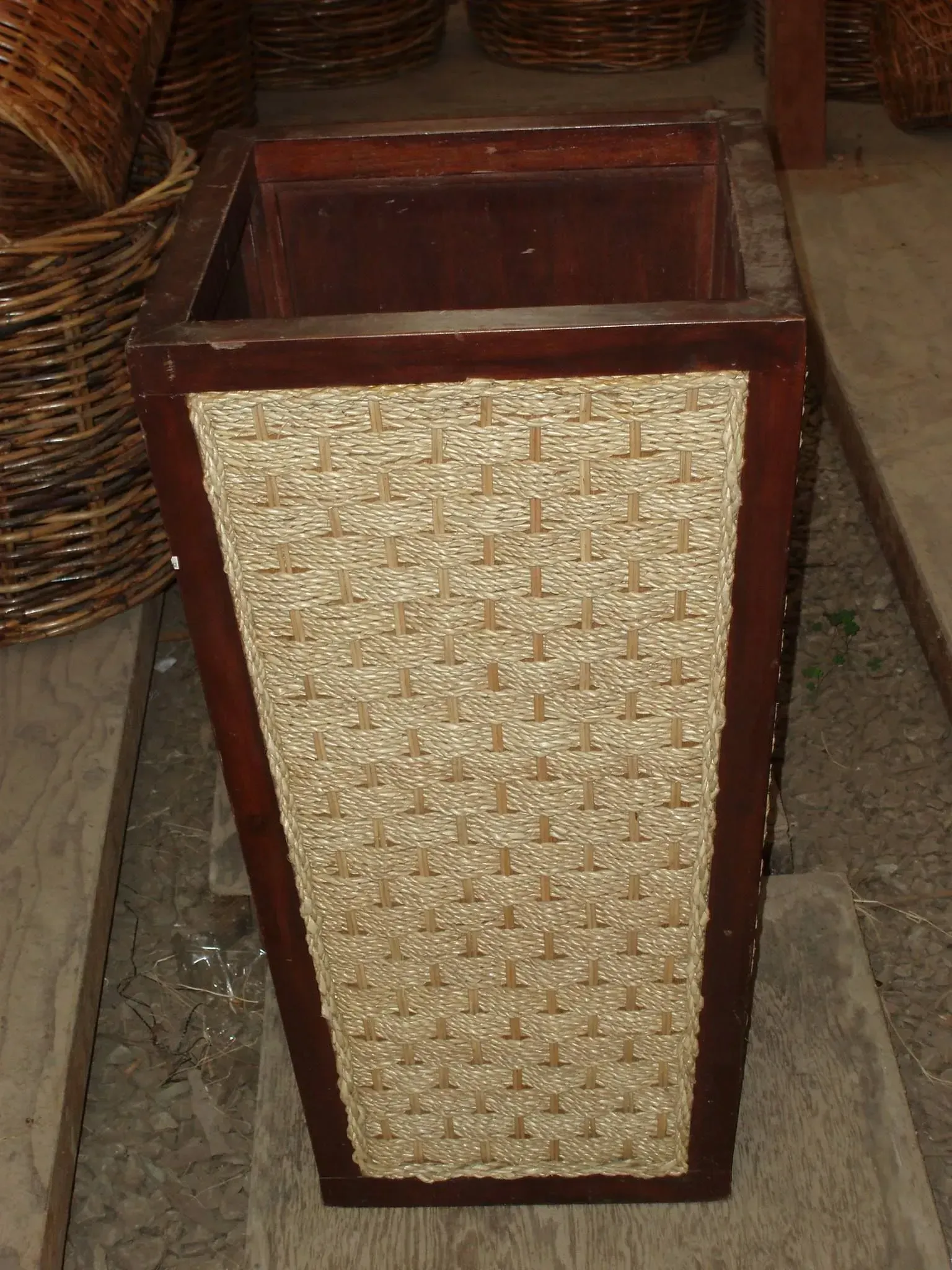 Tall, rectangular wooden planter with woven tan panels and dark wood trim, on a concrete surface.