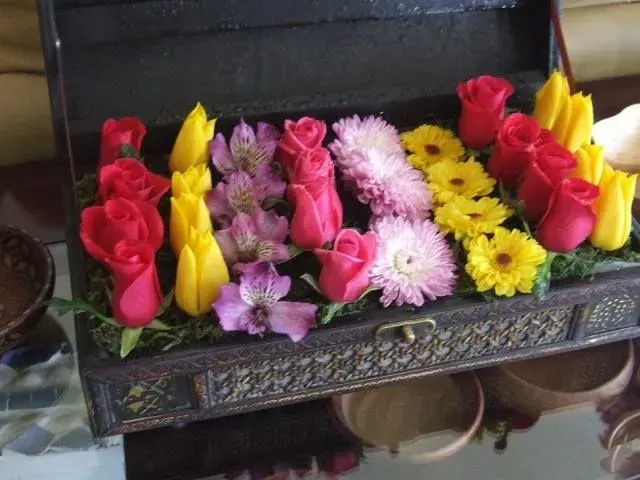 Floral arrangement in a decorative wooden box. Roses, tulips, and daisies in various colors.