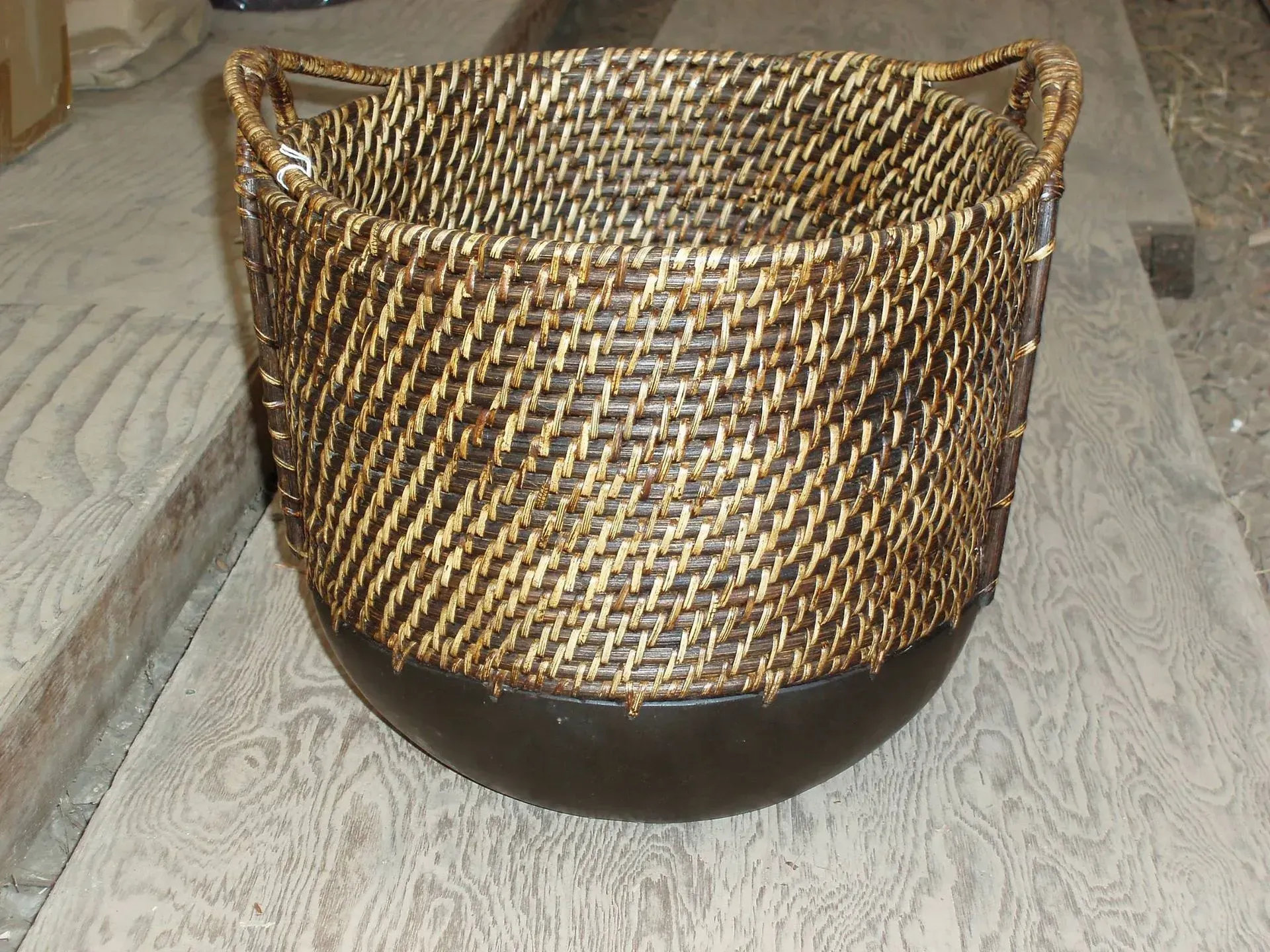 Woven rattan basket with a dark, rounded base and handles on a wooden surface.