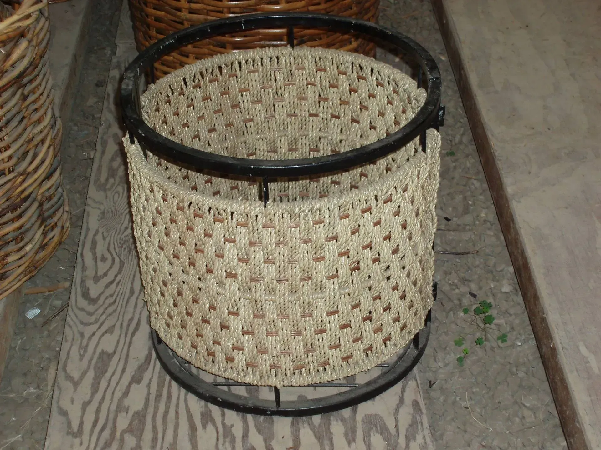 Tan woven basket with a black metal frame, sitting on a wooden surface.
