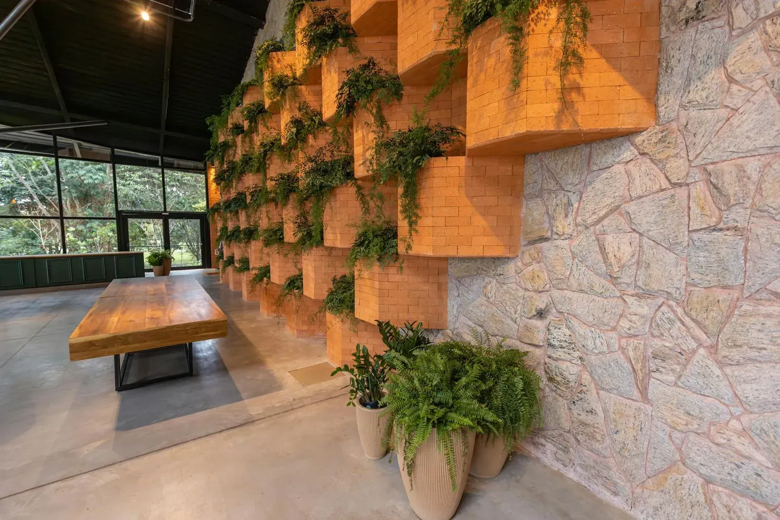 Interior with wooden table, green plants, and a wall with orange cubby holes and stone.