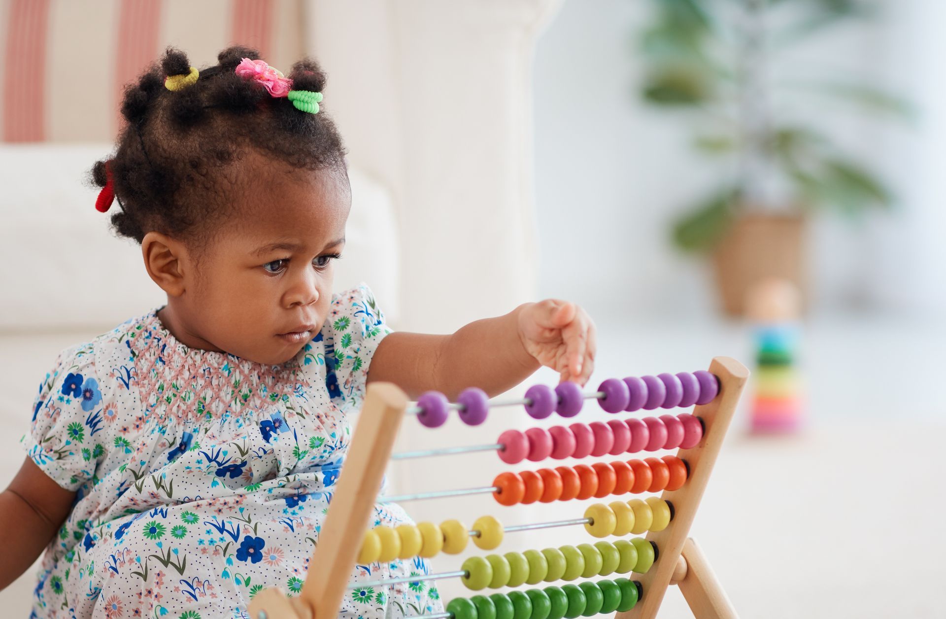 A little girl is playing with an abacus on the floor.