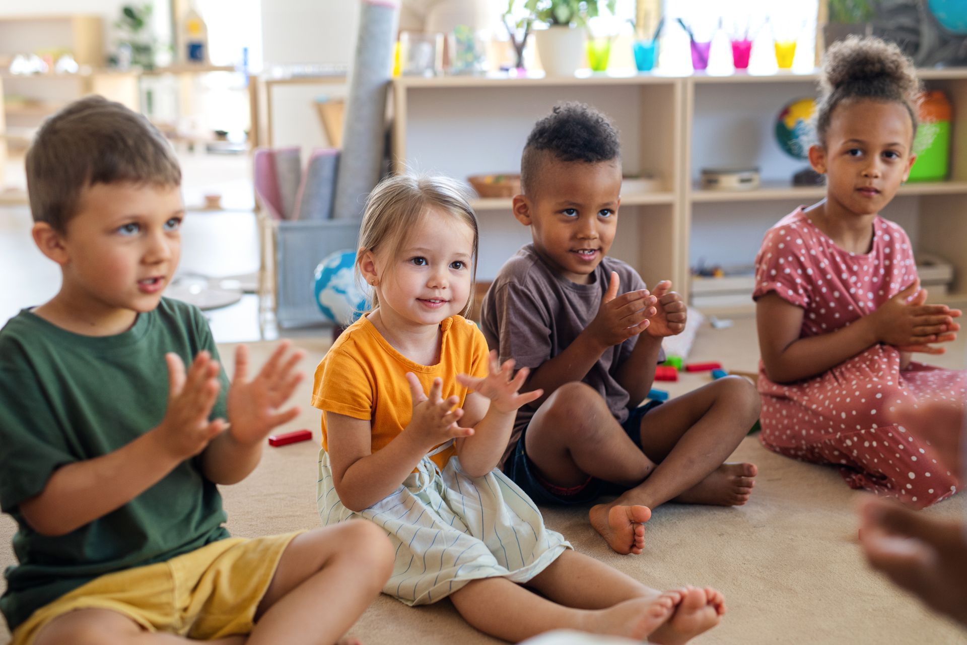 A group of children are sitting on the floor clapping their hands.