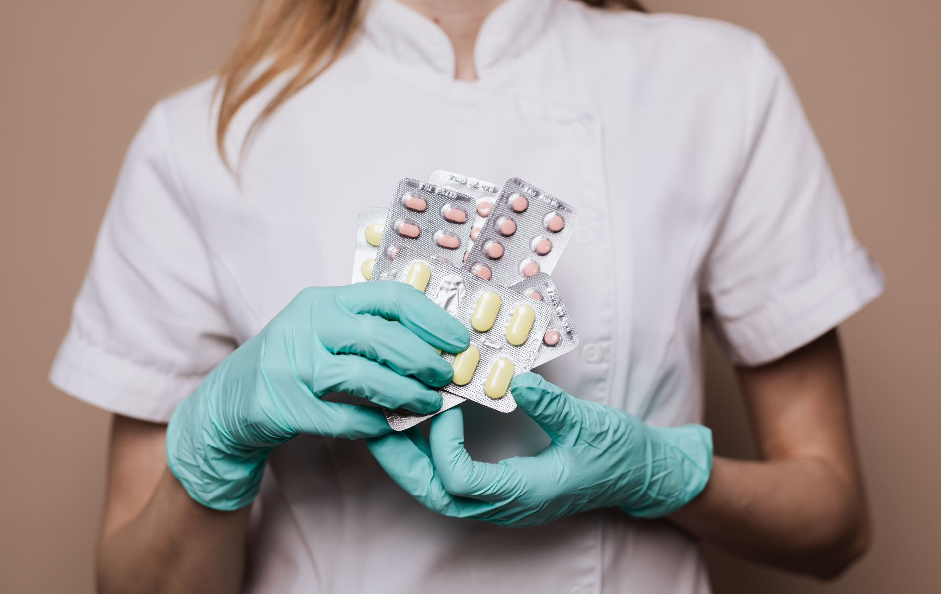 Person in white lab coat and blue gloves holding several blister packs of pills.