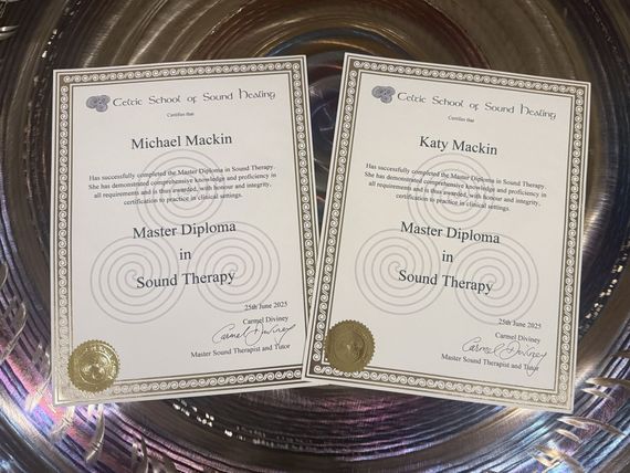 Two framed diplomas, for Michael Mackin and Kate Mackin, for Master Diploma in Sound Therapy, on a reflective surface.