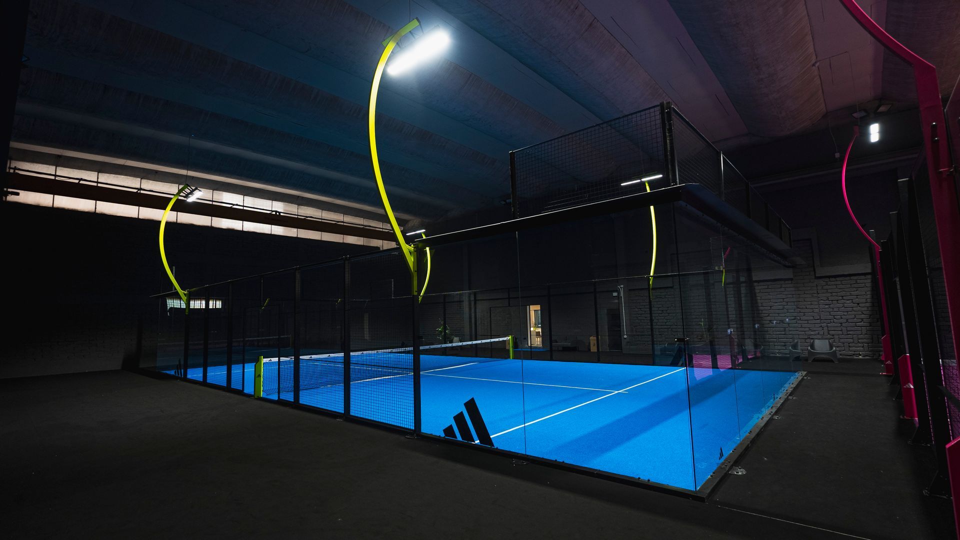 Campo da padel blu con pareti e tetto in vetro e una persona in piedi vicino all'ingresso.