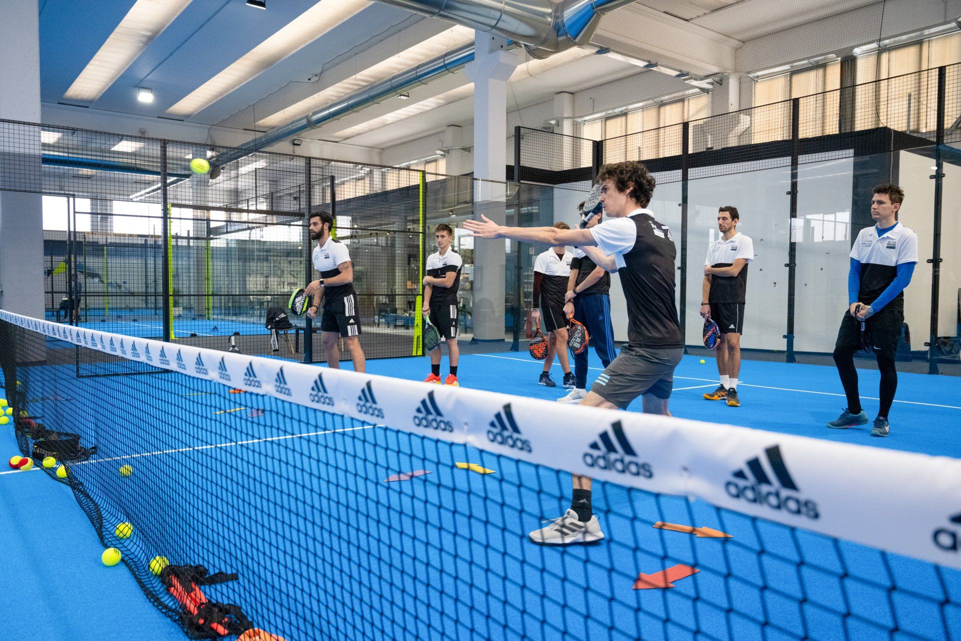 Persone che giocano a padel in un campo al coperto. Un giocatore lancia una palla oltre la rete