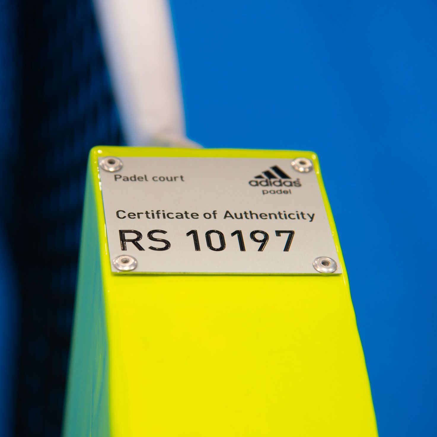 Primo piano di un pilastro da campo da padel giallo neon con il certificato di autenticità Adidas, numero di serie RS 10197.