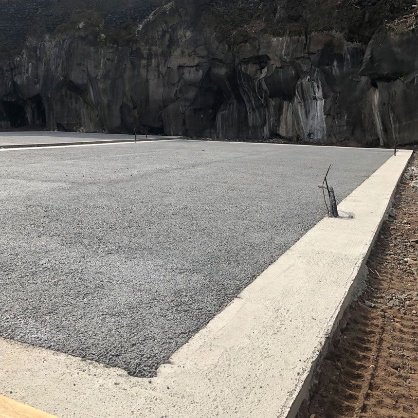 Superficie di ghiaia entro bordi di cemento, incastonata contro una parete rocciosa e scura.