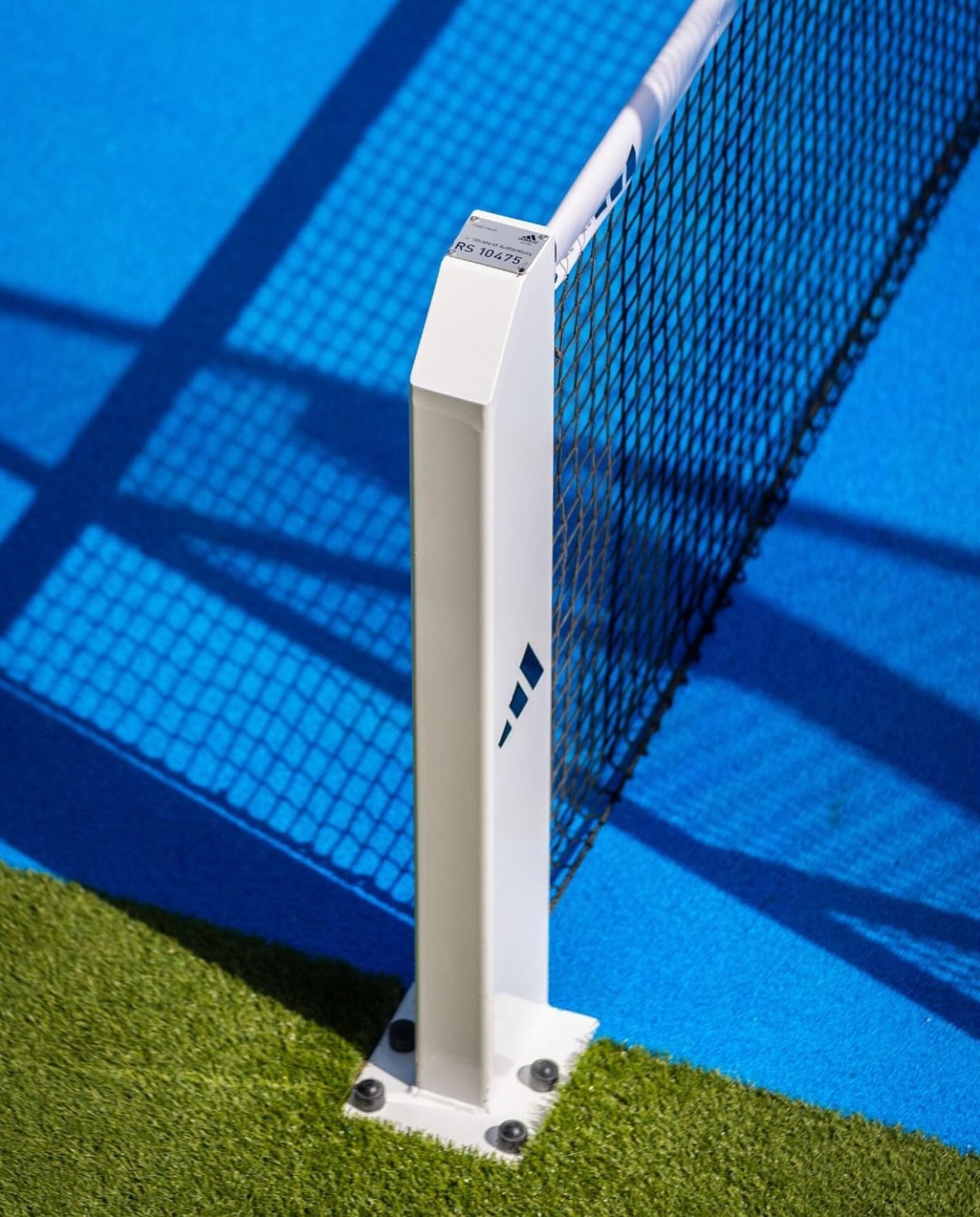 Palo bianco su un campo blu, bordo in erba verde. Ombre della rete e del palo.