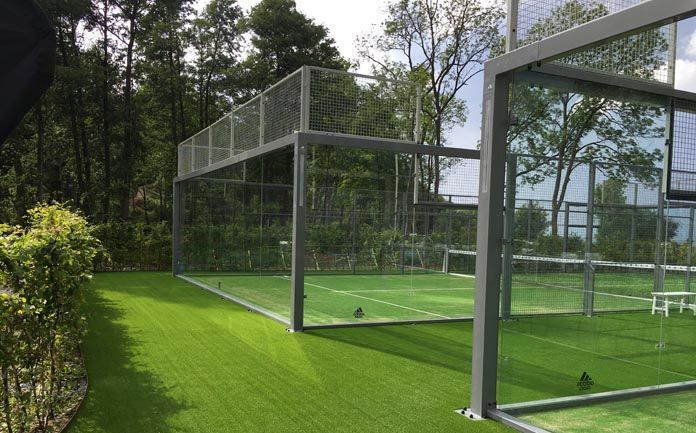 Campo da padel con erba sintetica verde e pareti in vetro, situato in un'area naturale e boscosa.