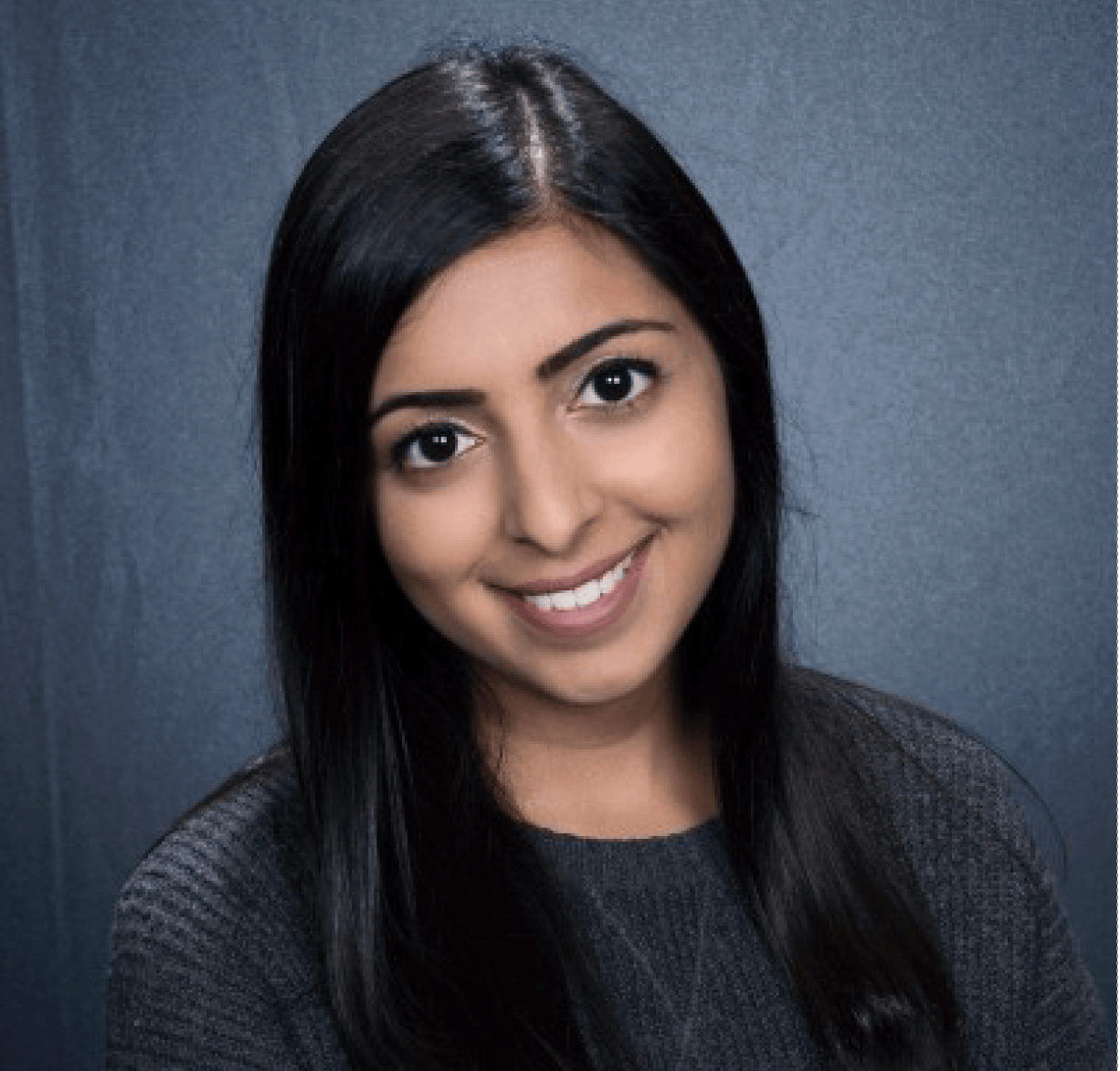 Woman with dark hair smiles, against a gray background, wearing a gray sweater.