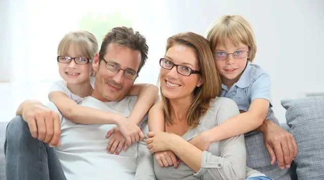 Family of four in glasses smiling, posing on a couch.
