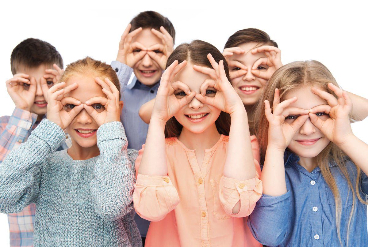 Group of children making eye-spy gestures with their hands, smiling at the camera.