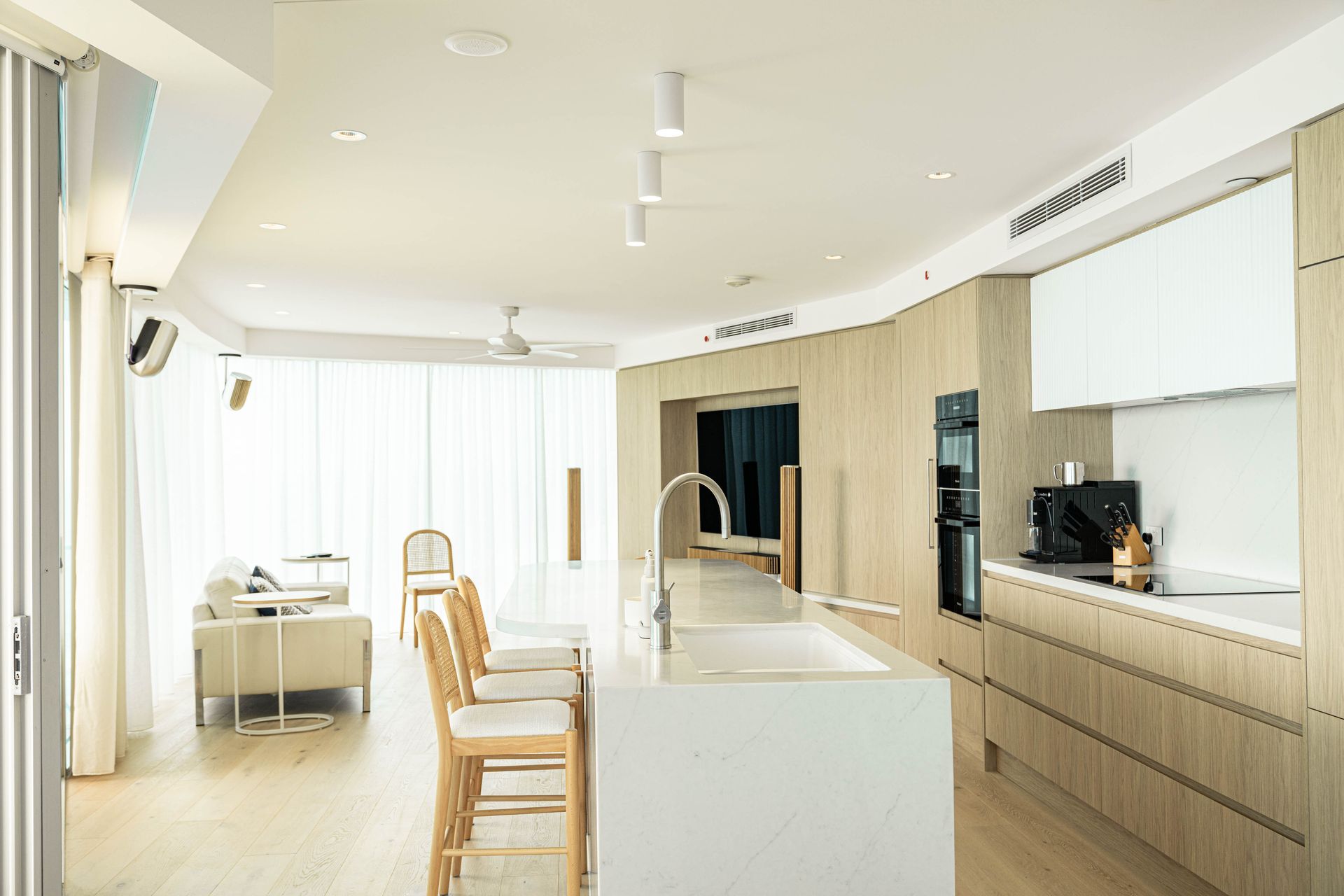 A Modern, Minimalist Kitchen With Light Wood Cabinetry, and an Adjacent Living Area — Elite Stone in Tweed Heads South, NSW