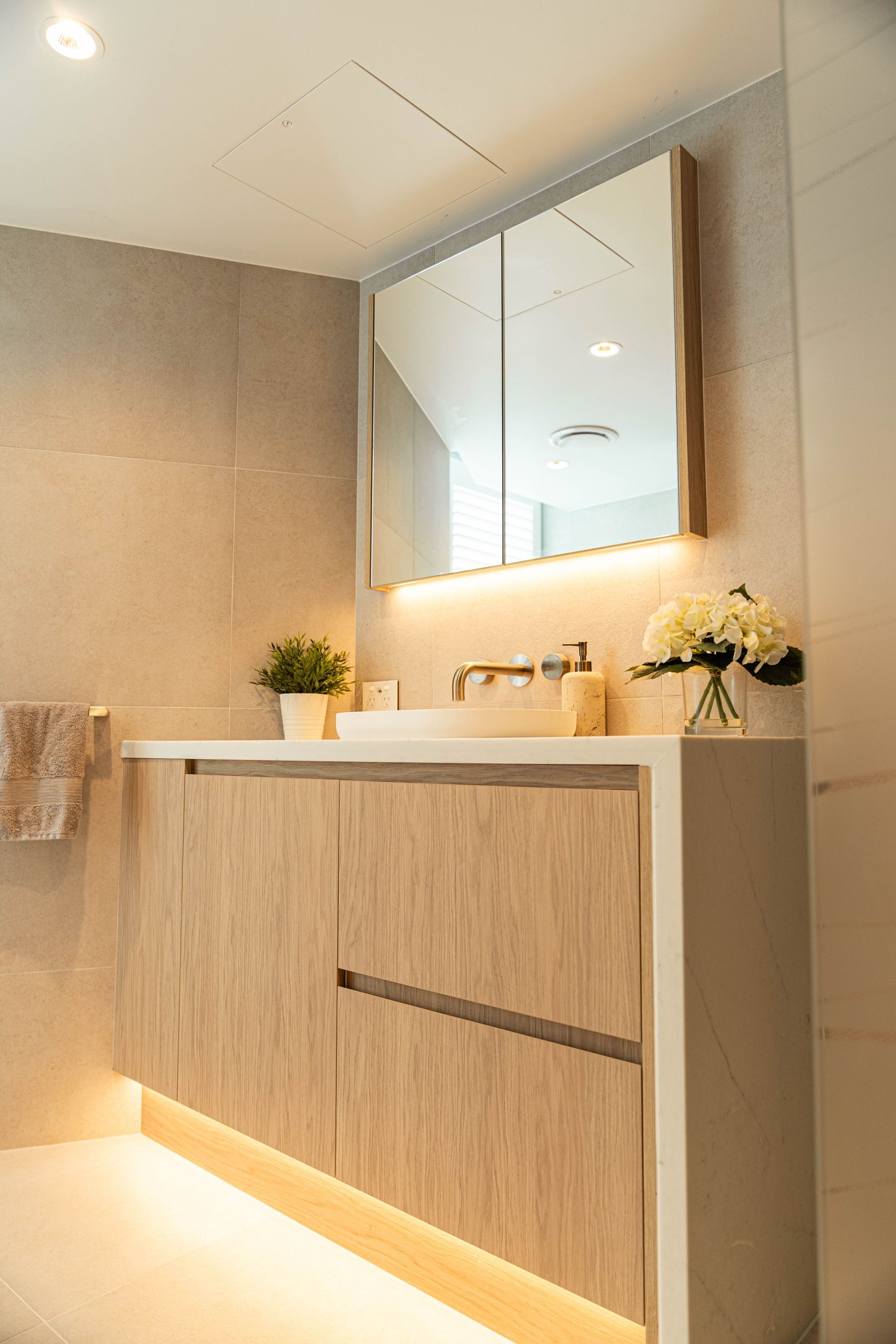 Modern bathroom vanity with a light wood cabinet, undermount sink, mirror, and warm under-cabinet lighting.