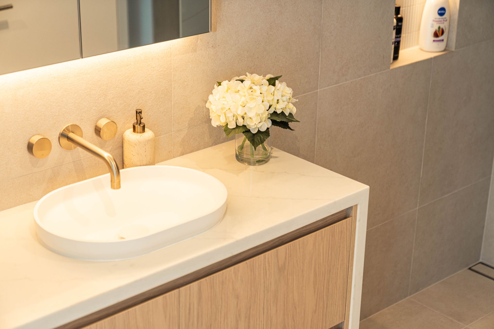 A Modern Bathroom Vanity Featuring a White Oval Sink and a Small Vase of White Flowers — Elite Stone in Tweed Heads South, NSW