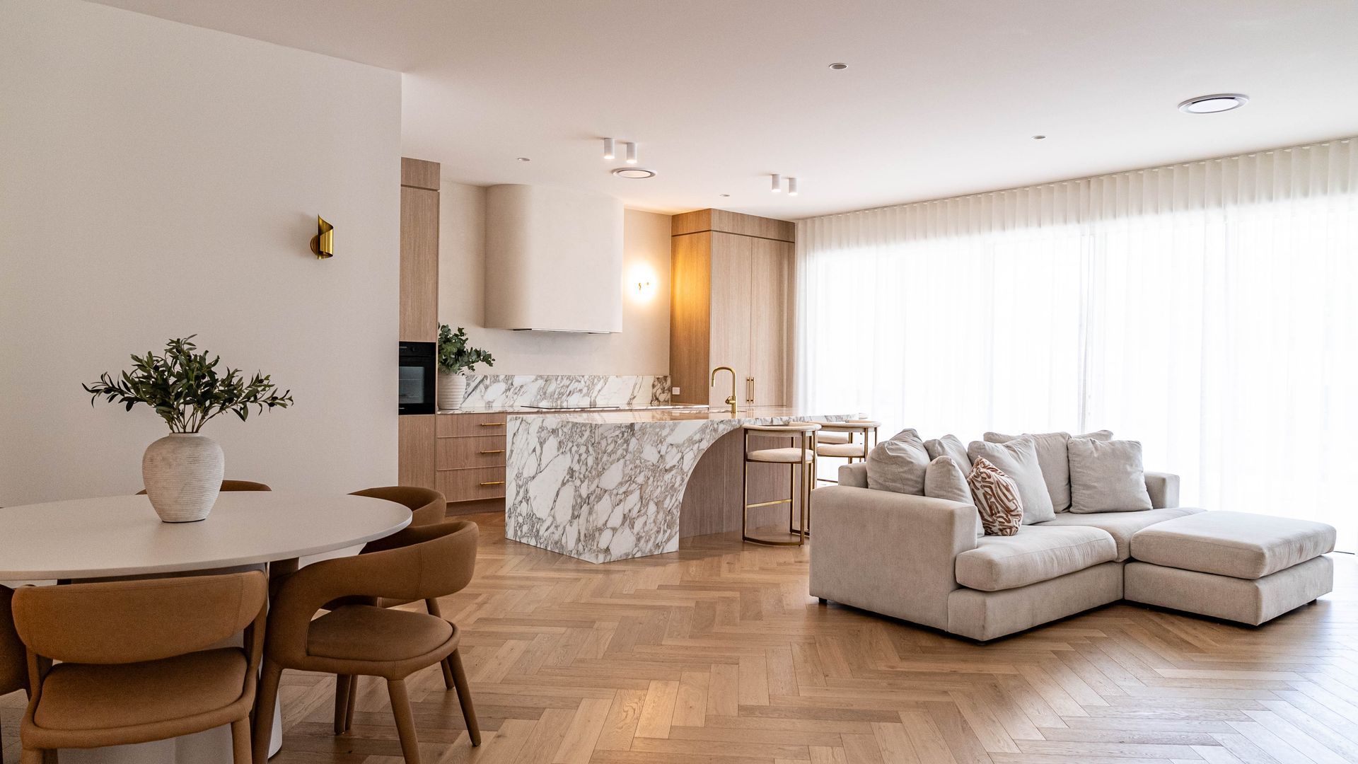 An Open-concept Living Space With a Round Dining Table and a Beige Sectional Sofa — Elite Stone in Tweed Heads South, NSW