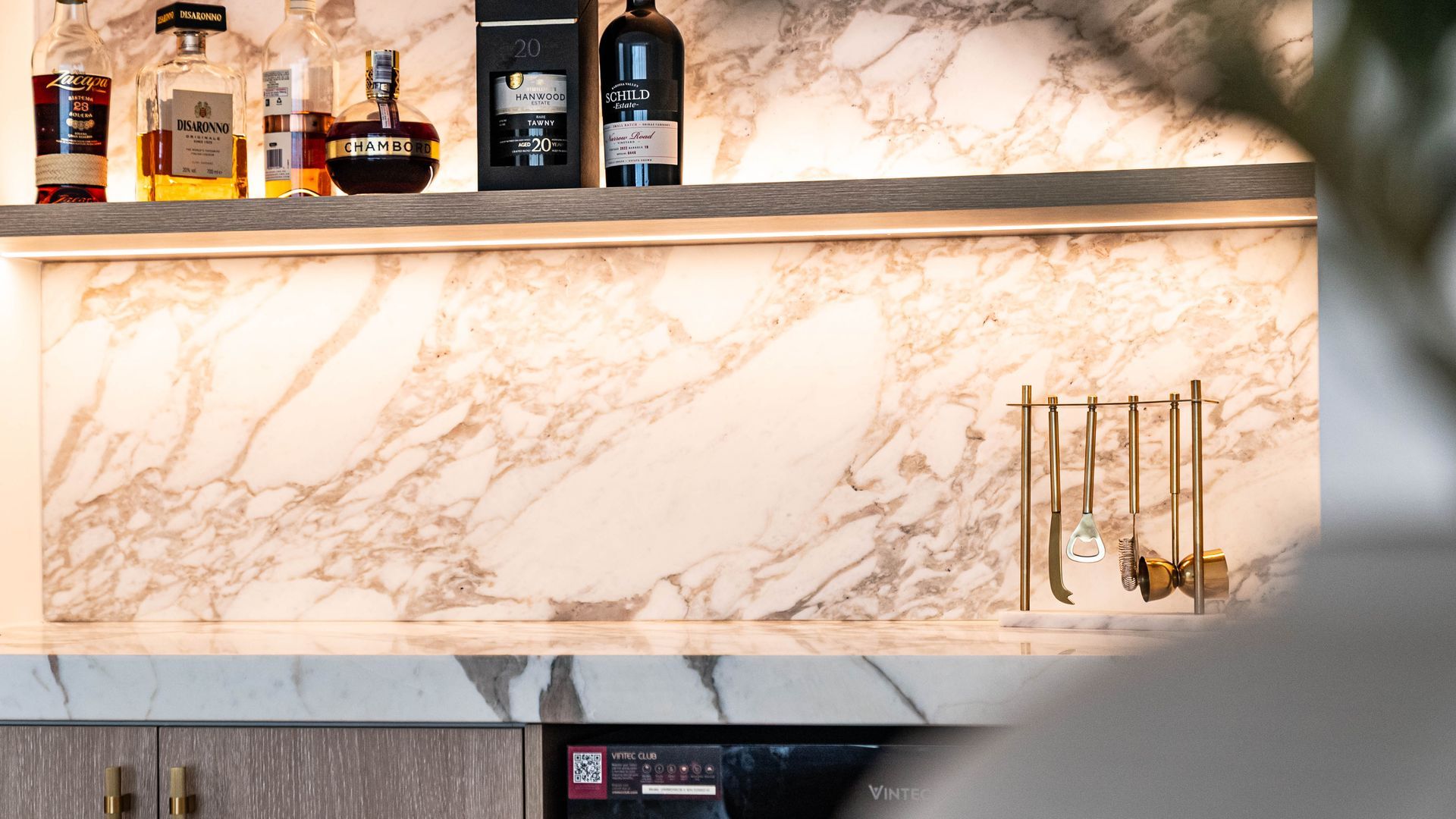 A Backlit Marble Backsplash Behind a Bar Shelf With Various Liquor Bottles — Elite Stone in Tweed Heads South, NSW