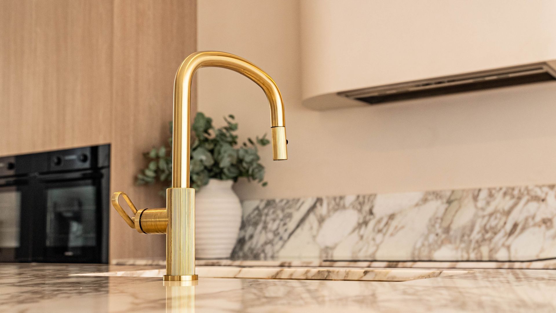 A Gold Kitchen Faucet Stands on a Marble Countertop With a Oven in the Background — Elite Stone in Tweed Heads South, NSW