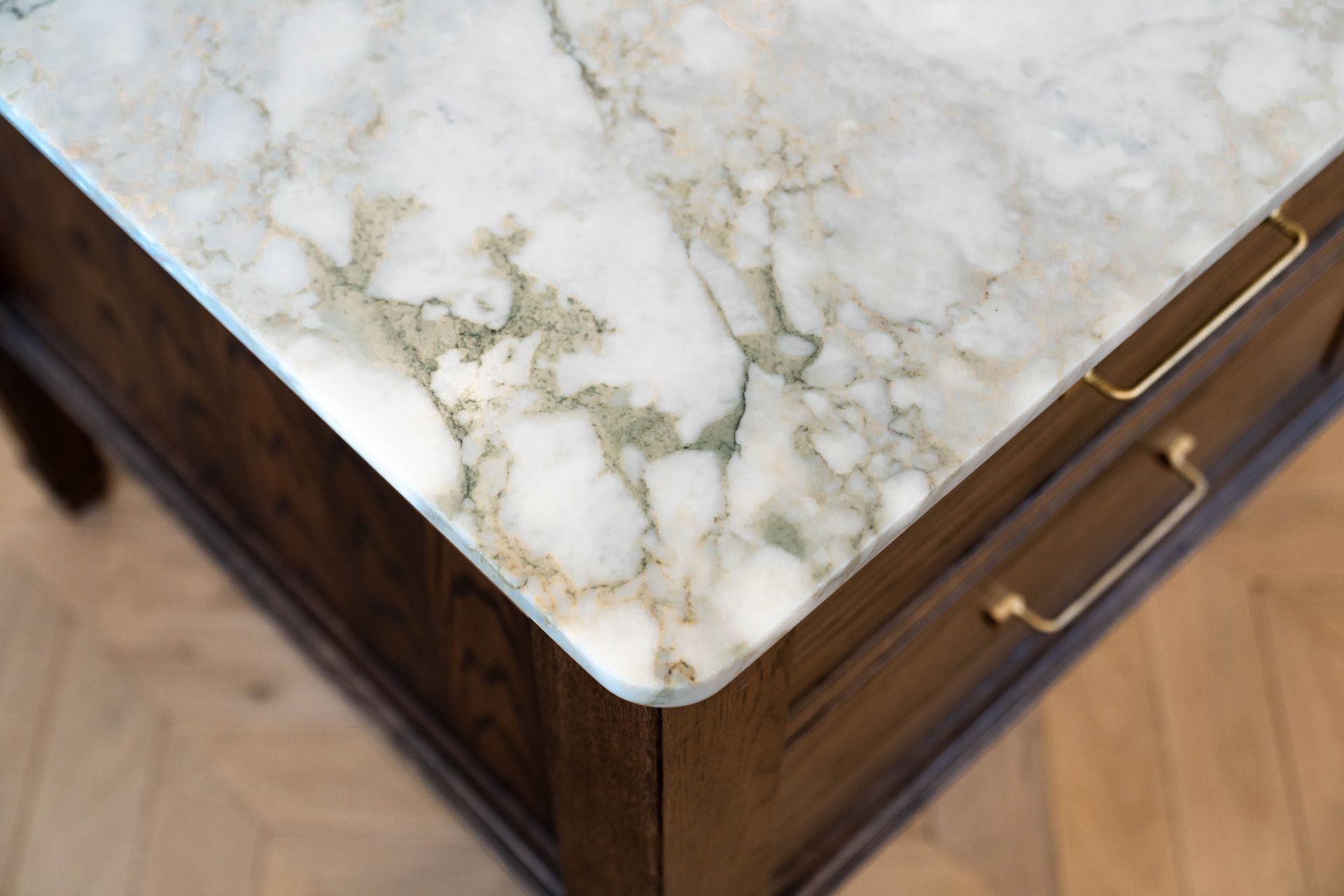 A high-angle view of a wooden cabinet with a white and gray marble countertop and brass drawer handles.