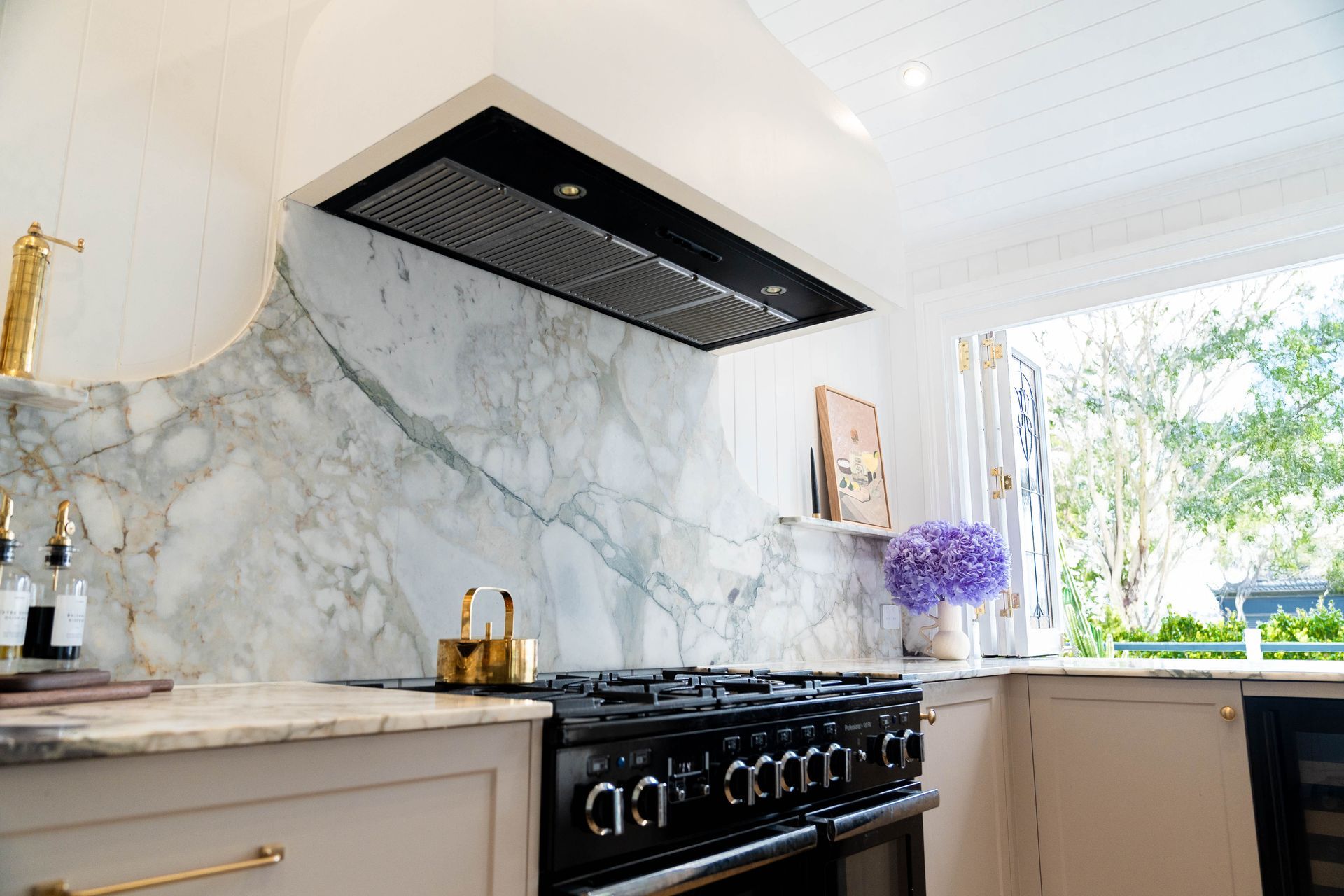 A modern kitchen featuring a black range stove, a matching range hood, and a dramatic white-and-grey marble backsplash.