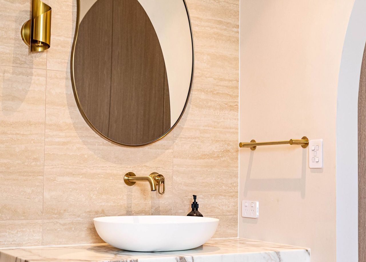 Modern Beige Bathroom With Oval Mirror, Gold Fixtures, And White Vessel Sink