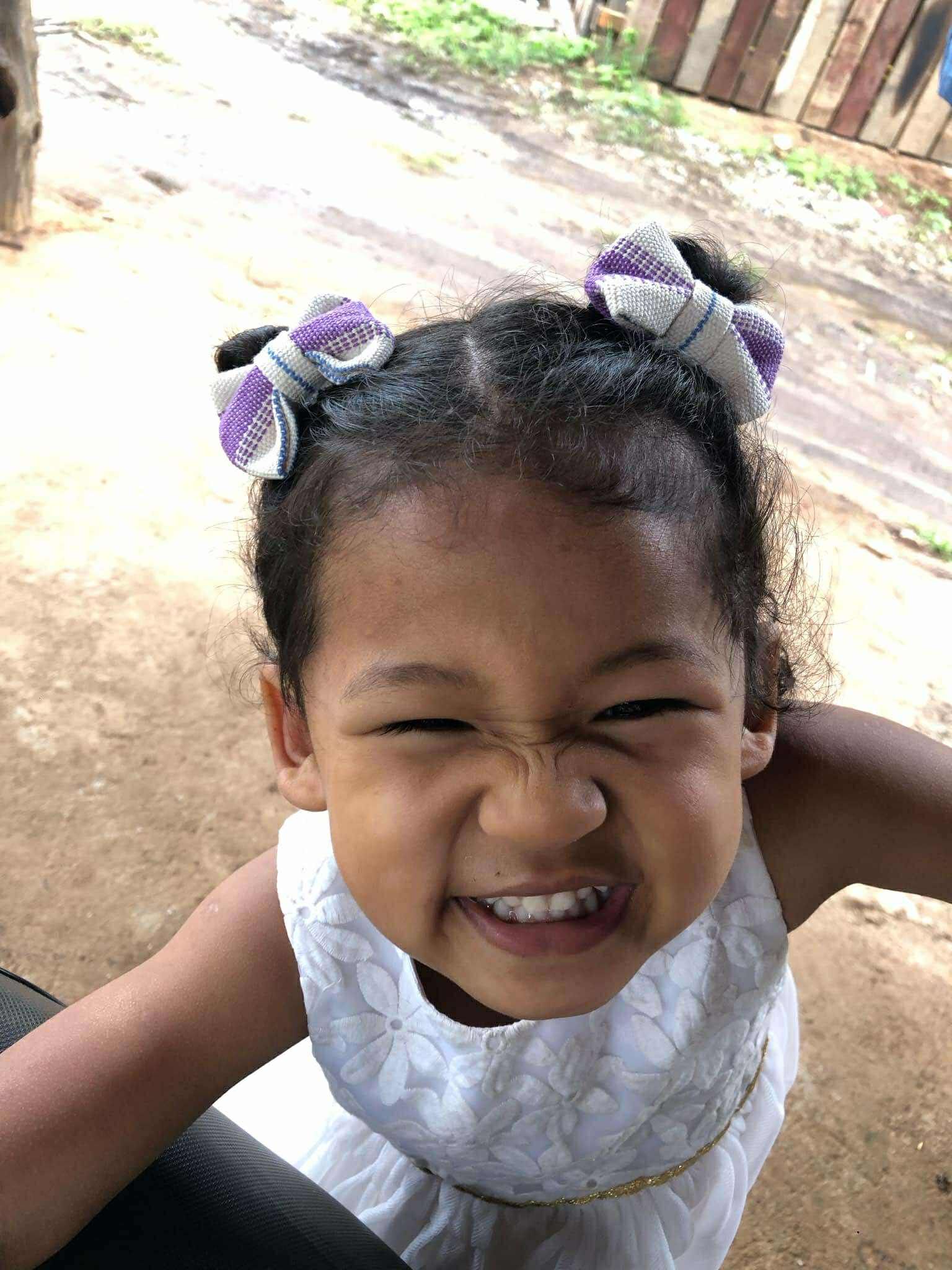 A little girl in a white dress is smiling and making a funny face.