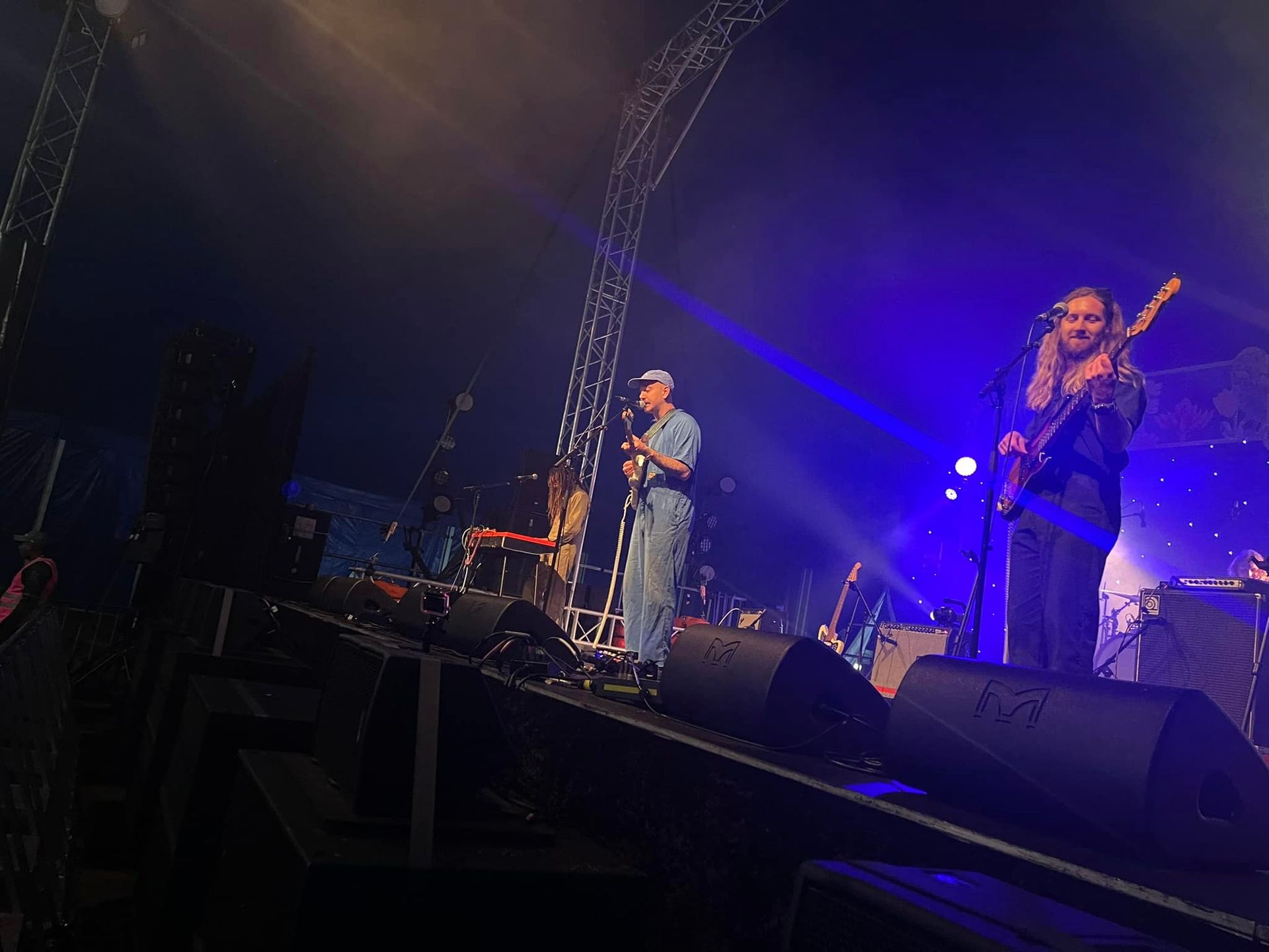 A band performs on stage under blue lights. A singer holds a mic and a guitarist plays.