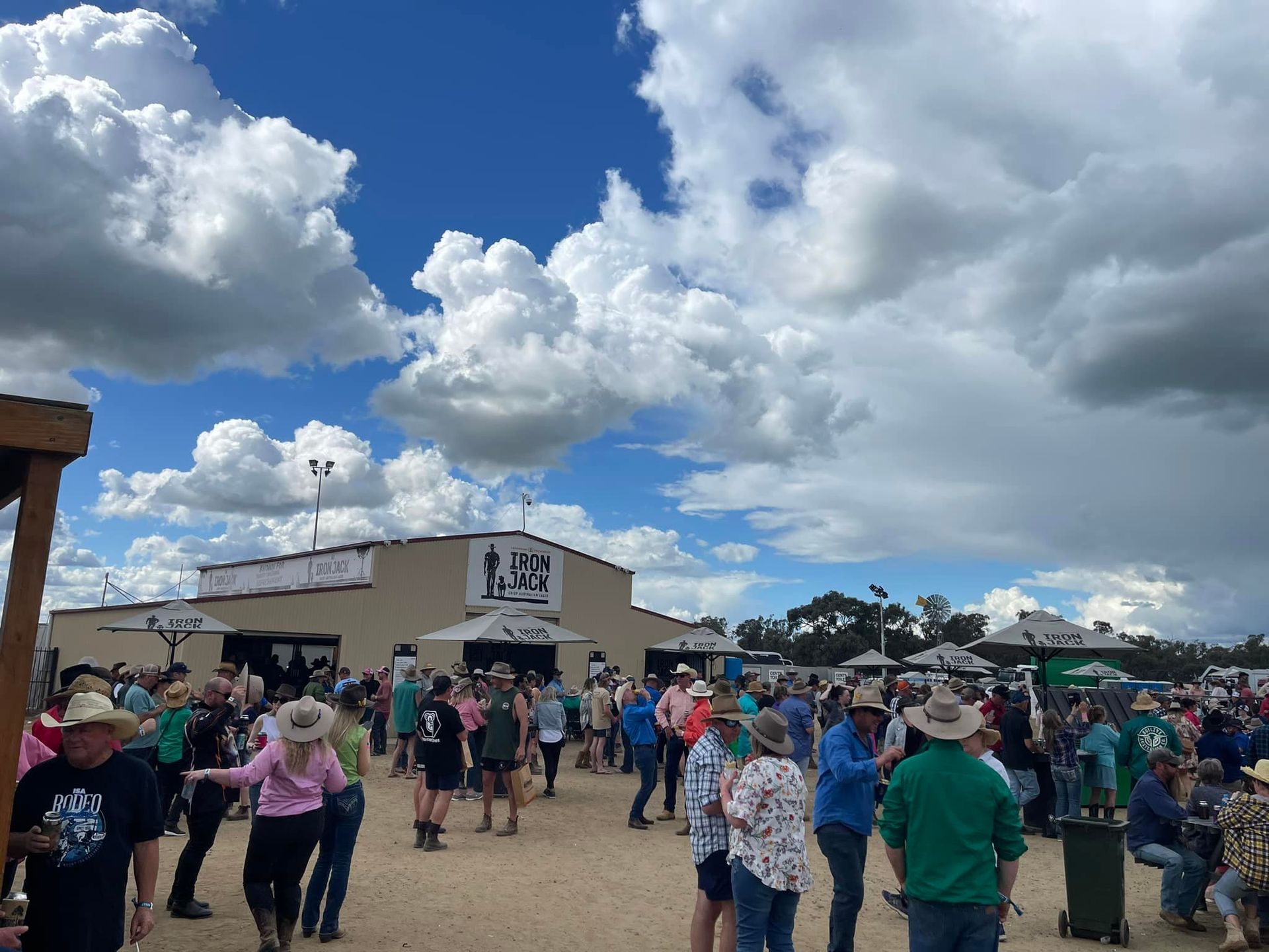Crowd at an outdoor event. People wear hats and casual attire, under a cloudy blue sky.