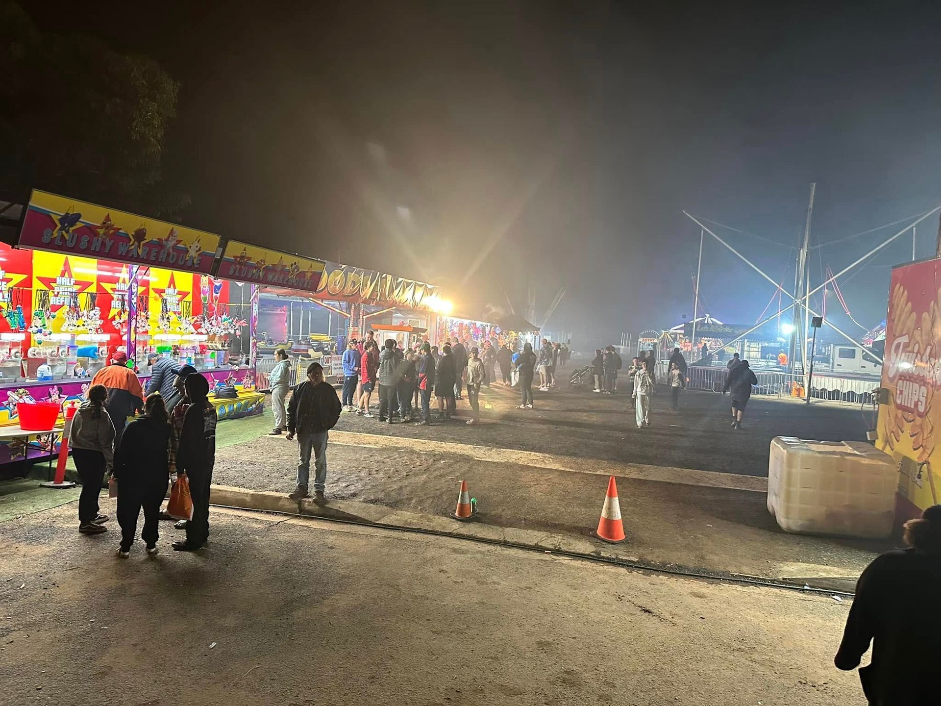 Night fair with crowds, colorful booths, and bright lights.