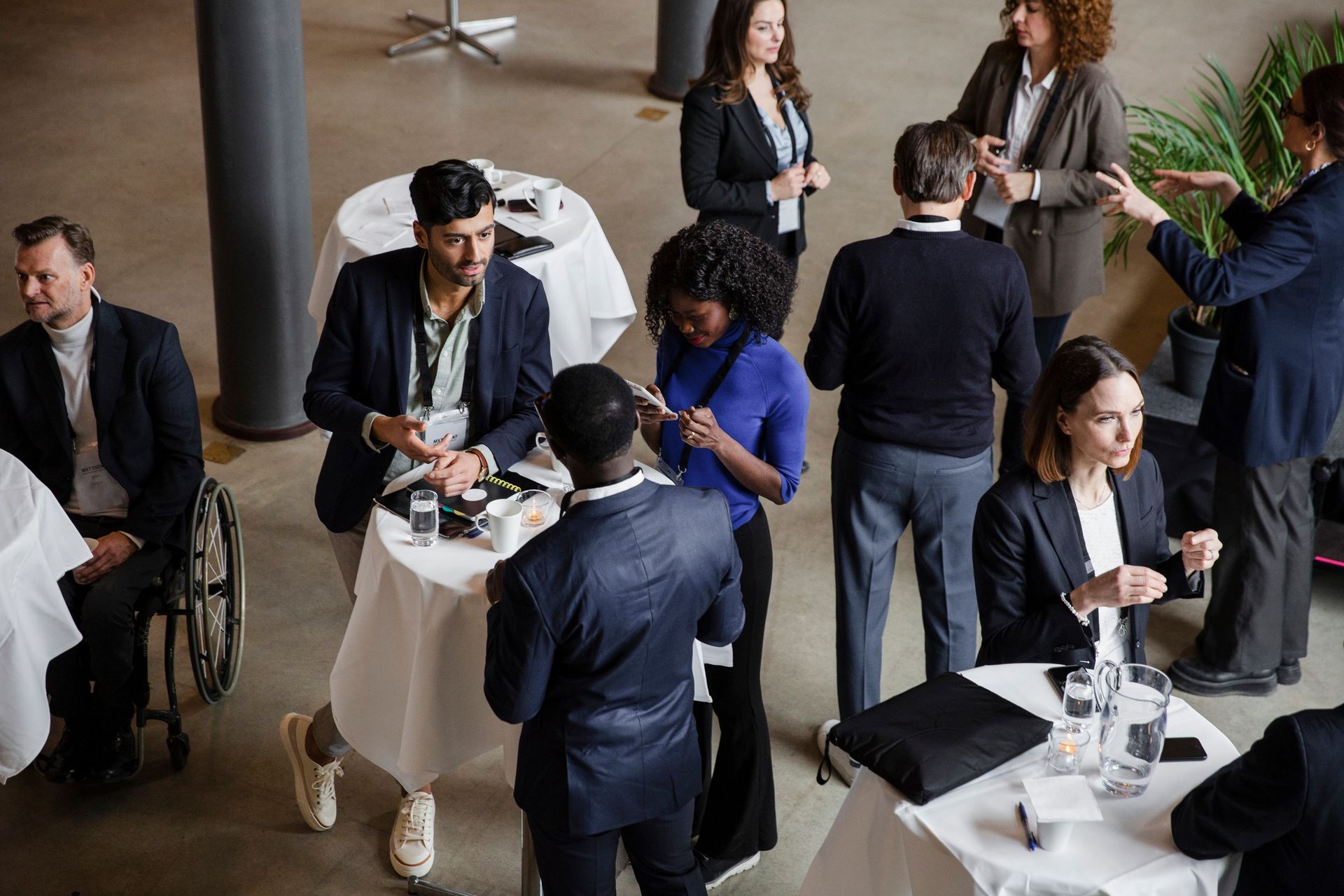 People networking at an event, gathered around small tables in a large room.
