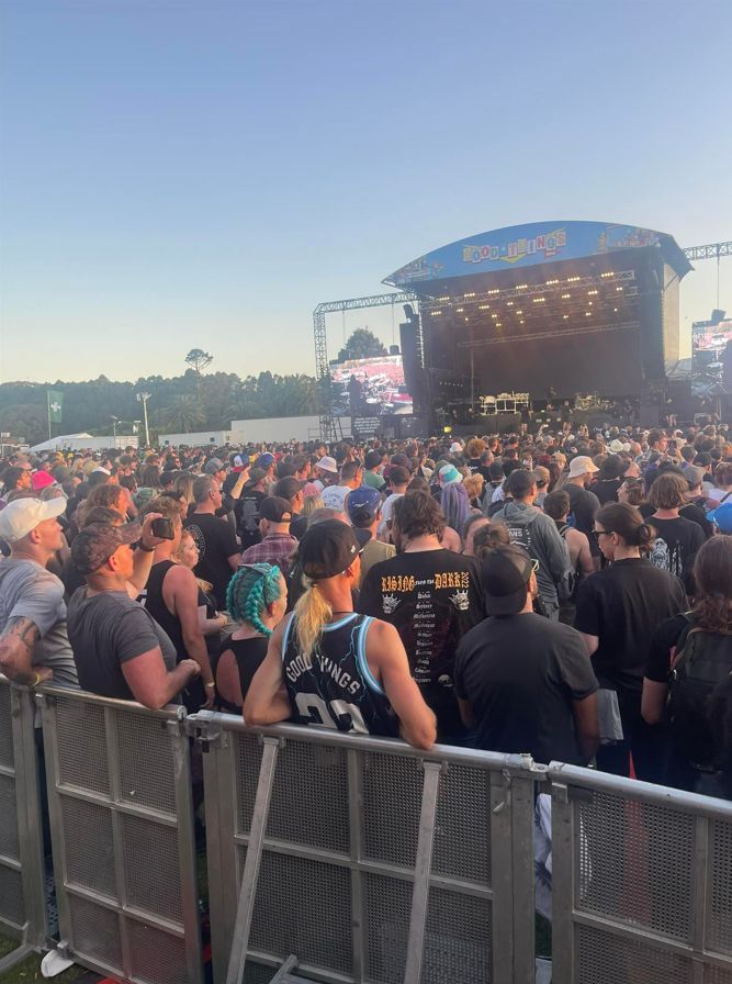 Crowd at an outdoor music festival, watching the stage. Many people, concert stage, sunny day.
